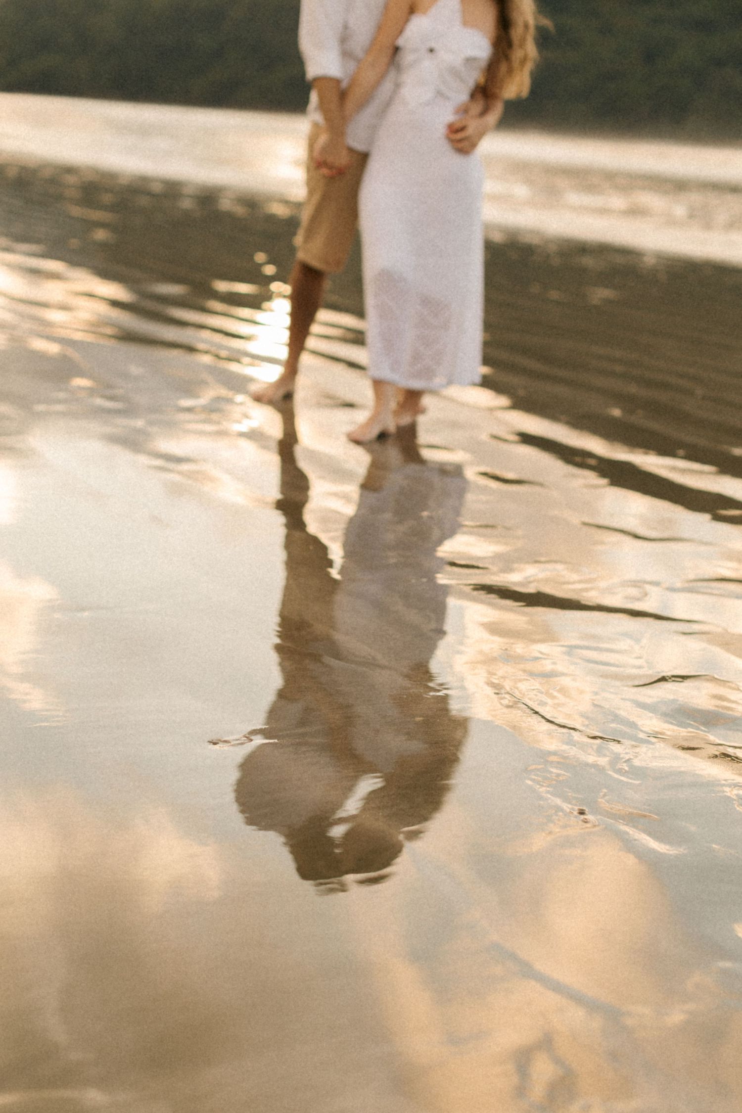 Reflections of feet in wet sand on a peaceful beach during golden hour.