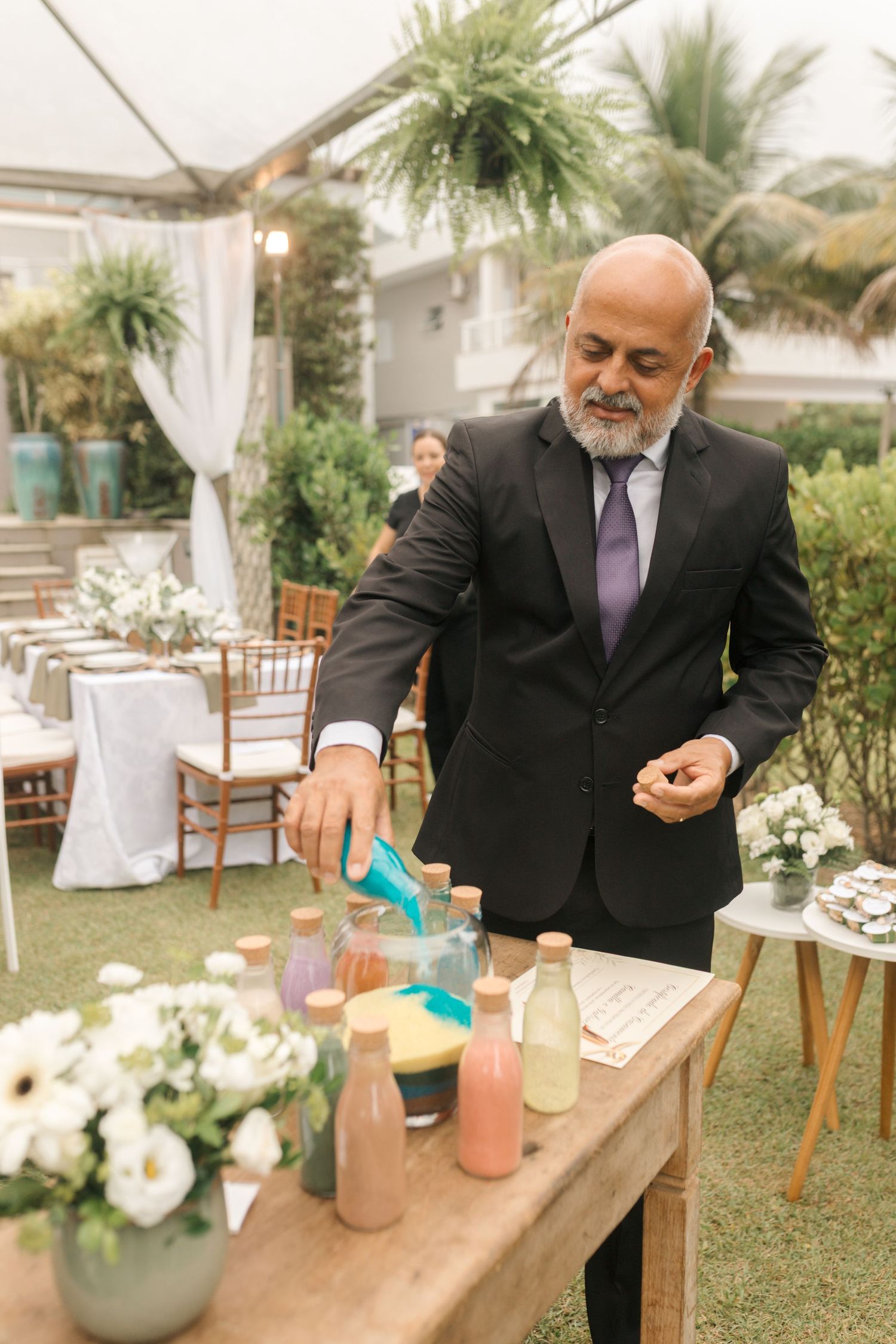 Wedding officiant preparing colored drinks for a unity ceremony at outdoor reception.