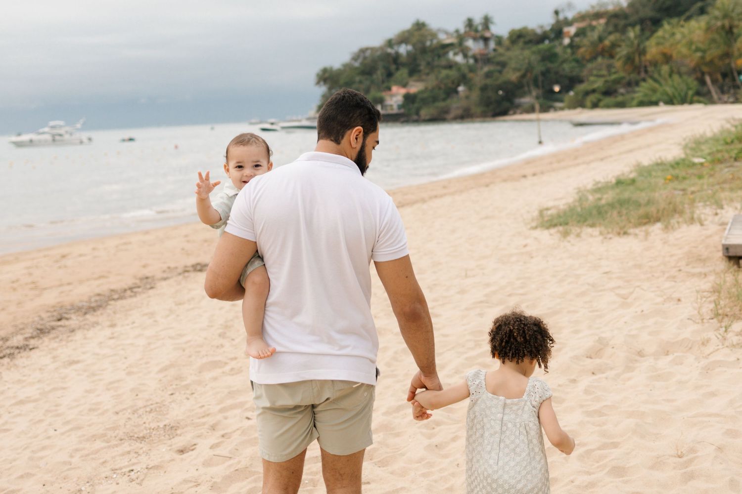 Family walking together along a scenic beach shoreline with lush greenery in the background.