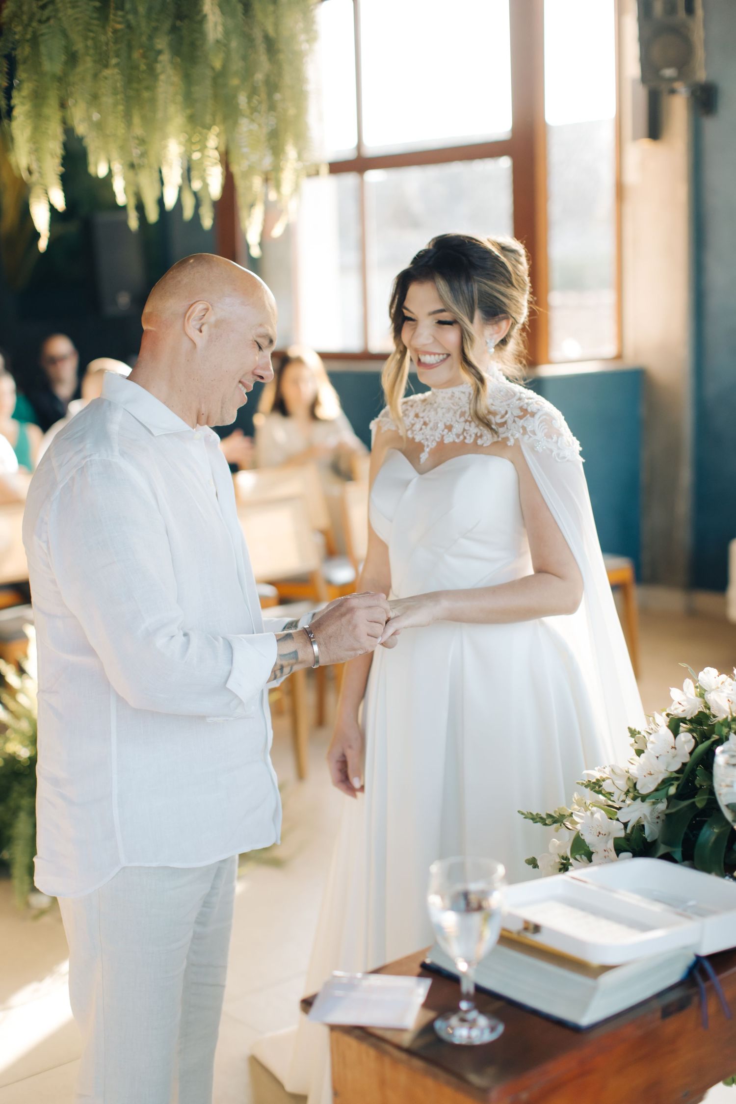 A tender moment during a wedding ceremony as the couple exchanges rings under hanging floral decor.