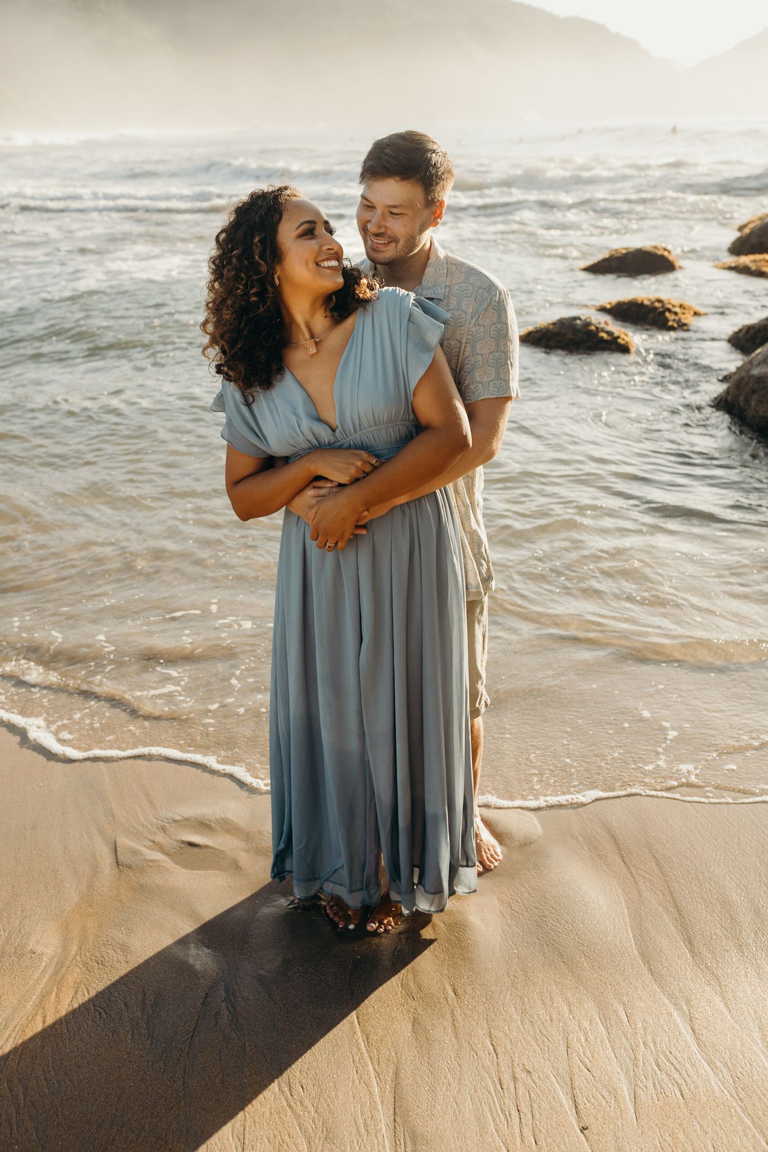 Happy couple embracing on a beach with gentle waves rolling in at sunset.