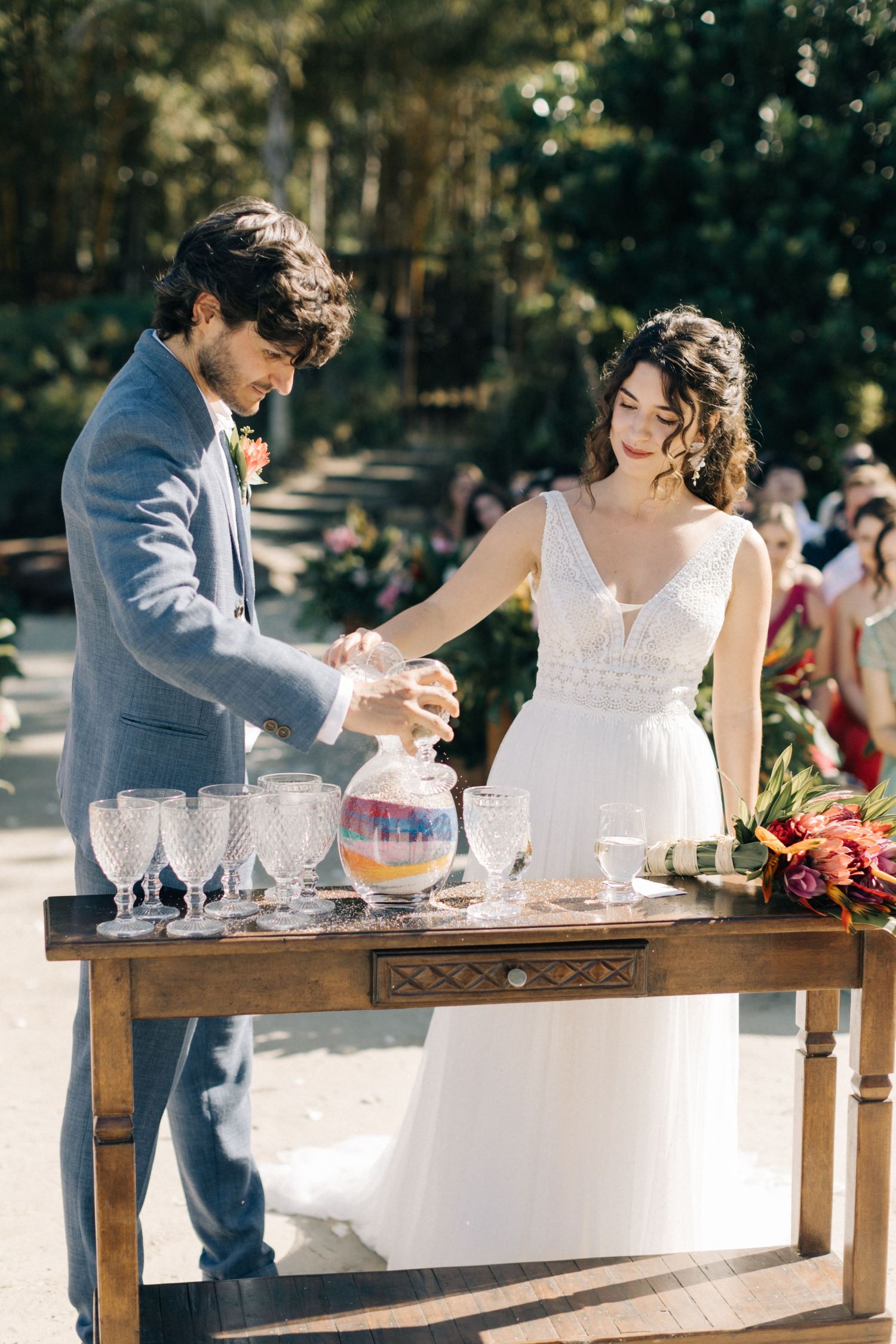 Newlyweds prepare drinks together at a rustic wooden bar during their outdoor reception.