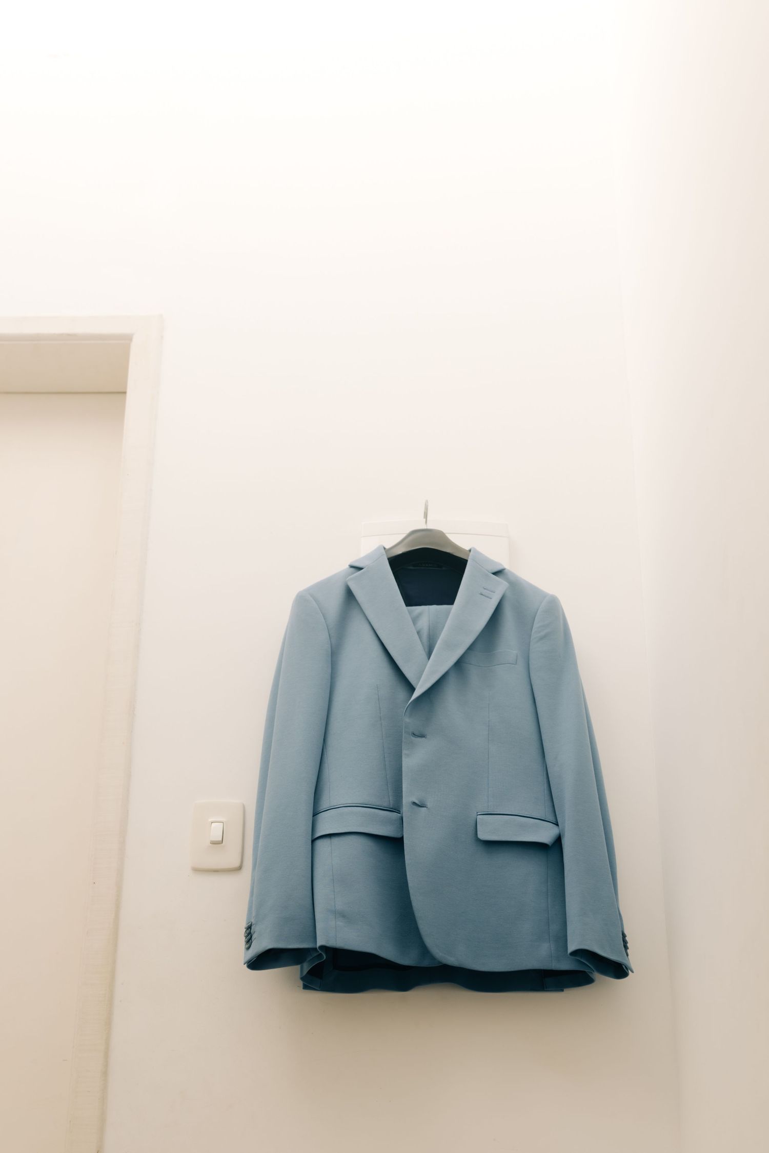 Light blue suit jacket hanging on display against white wall.