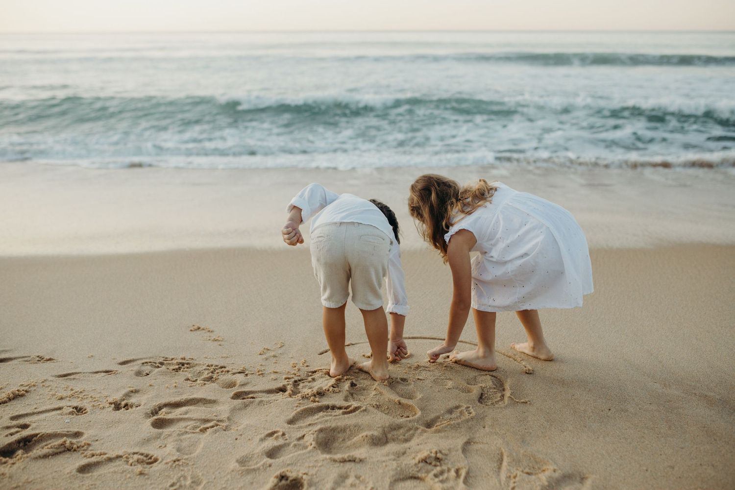 Children exploring the sandy beach together while ocean waves wash ashore.