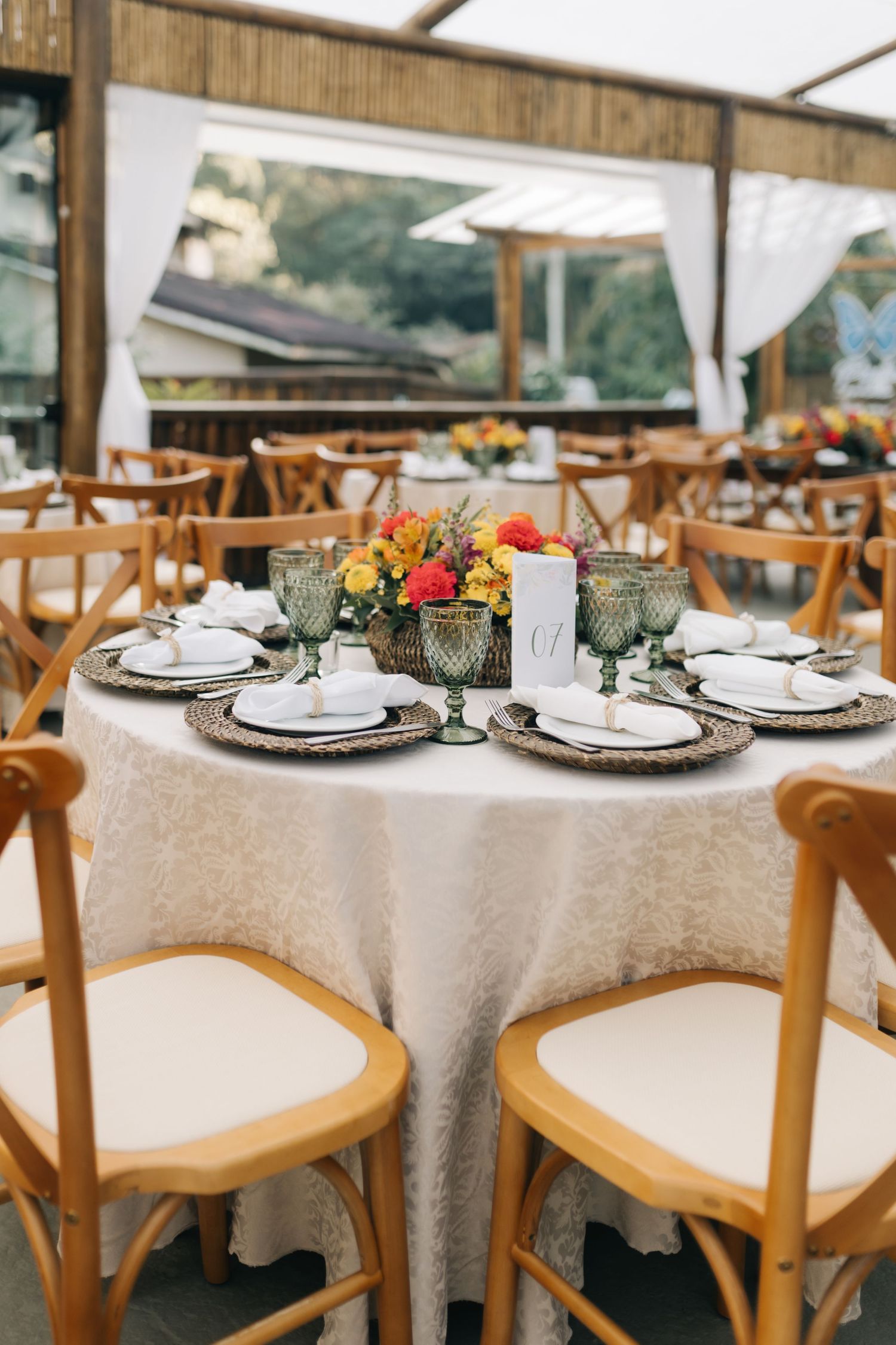 Elegant wedding reception tables set with white linens, wooden chairs, and place settings in a rustic indoor venue.
