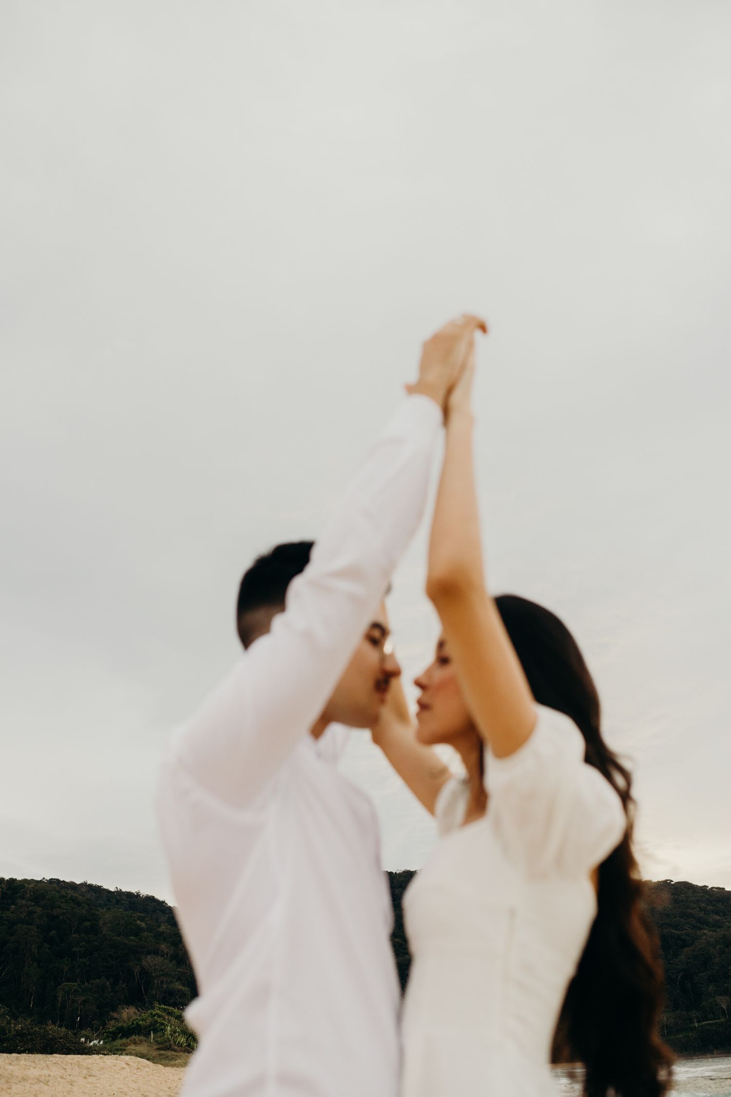 A couple raises their hands together in celebration on a scenic beach.