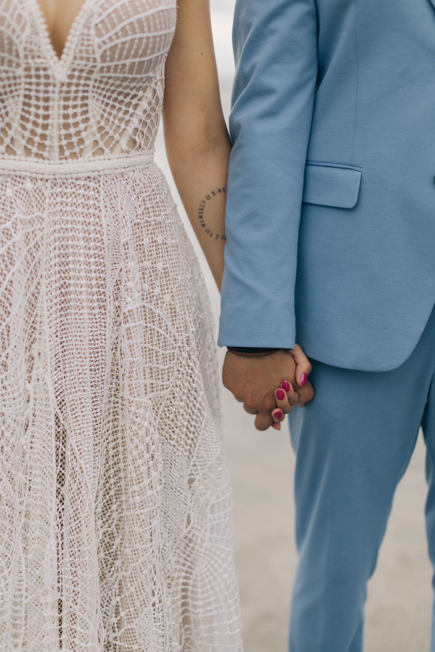 Close-up detail of a couple holding hands, showing lace dress and blue suit.