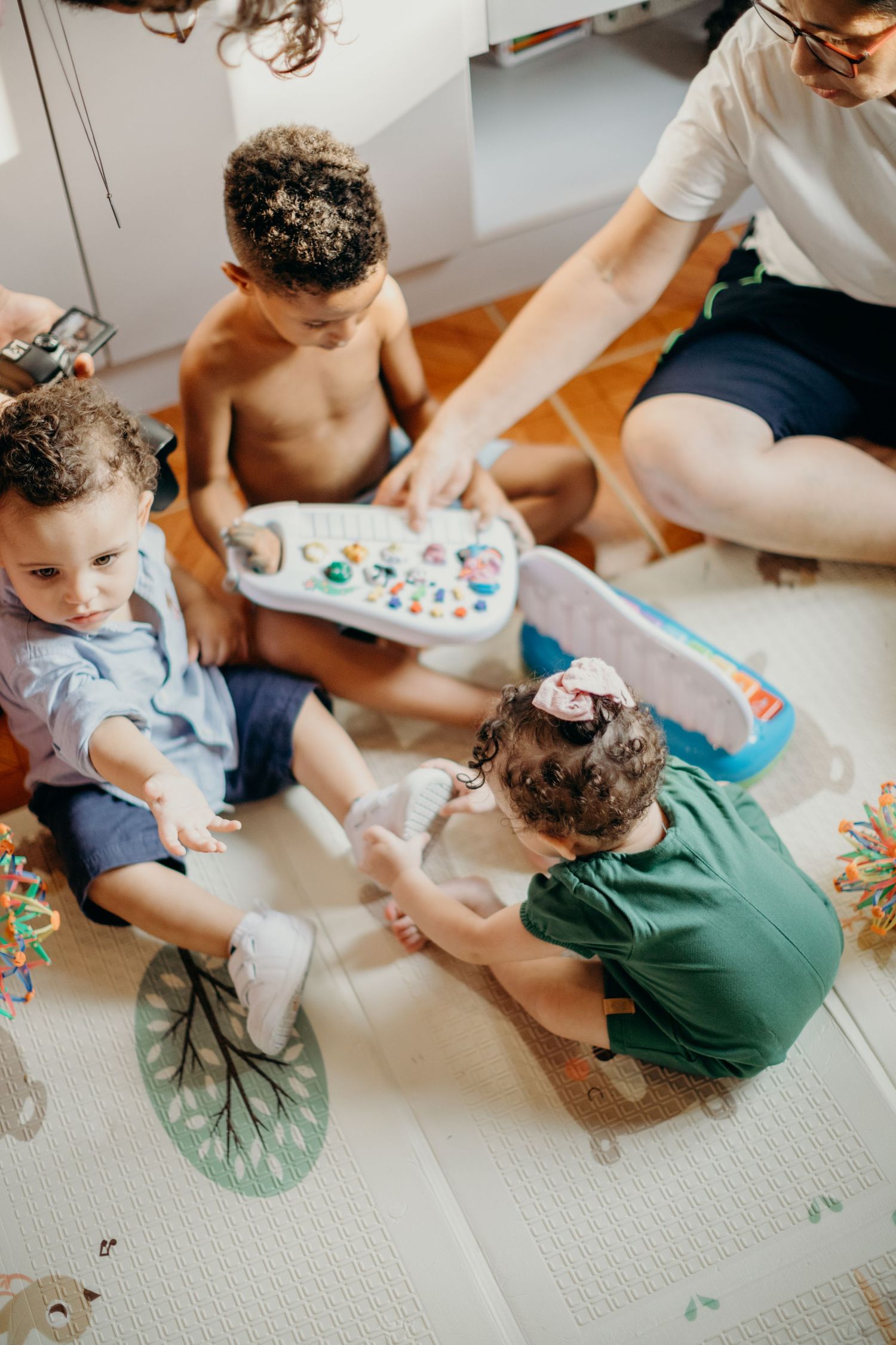An overhead view of a family playtime session with toys on a patterned floor mat.