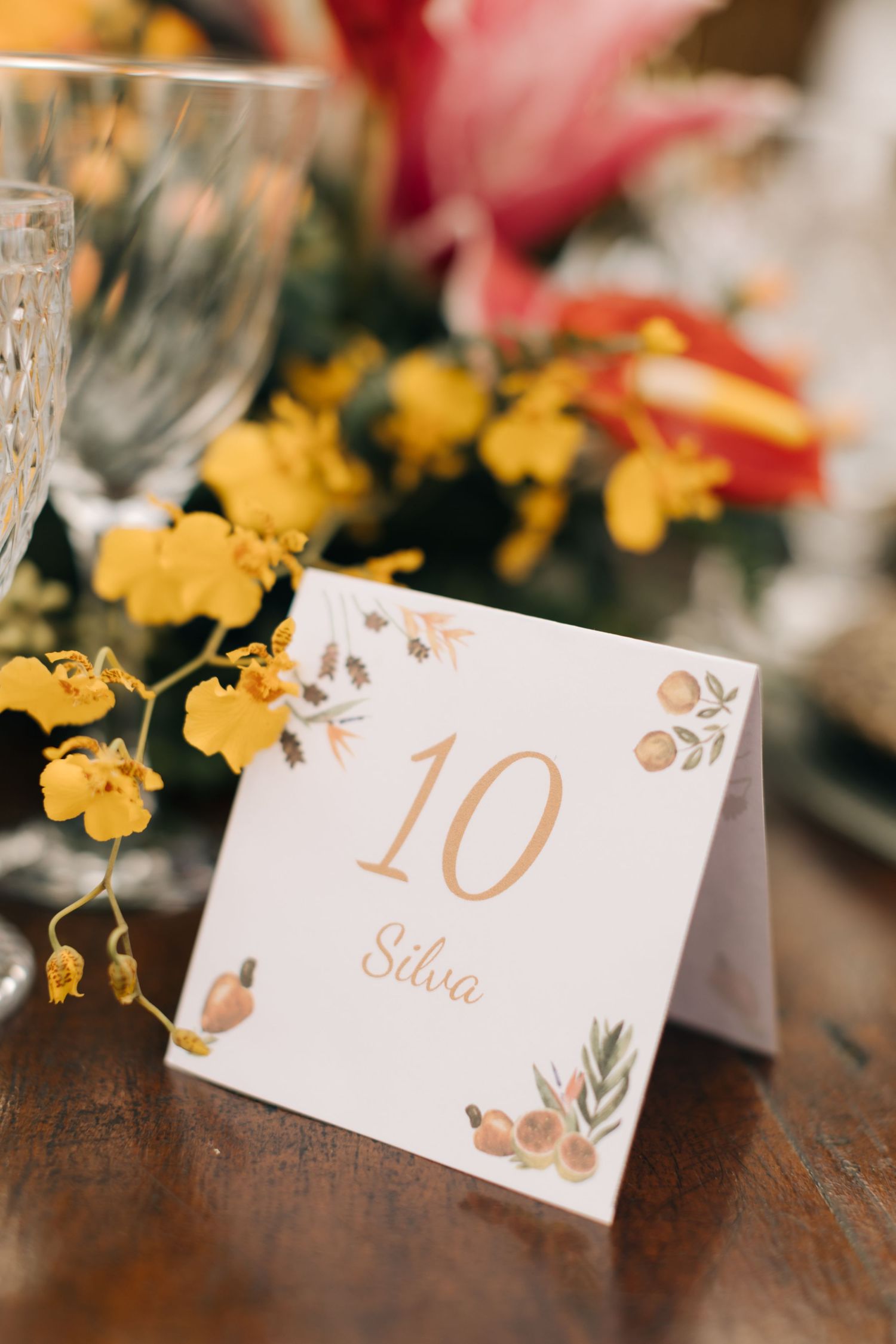 Elegant wedding table number ten card with floral design in gold lettering against blurred flowers.