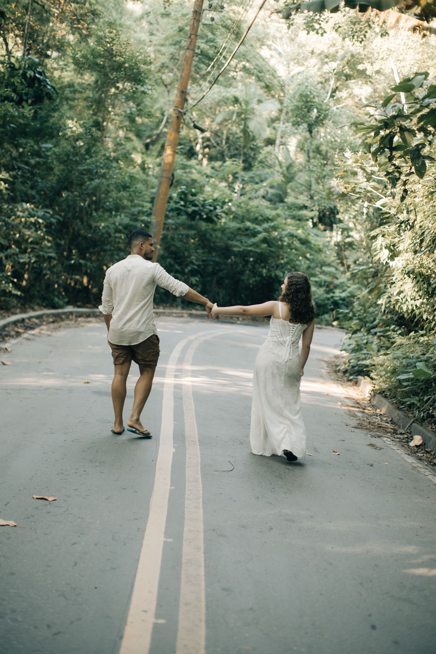 A couple holding hands while walking down a tree-lined road.