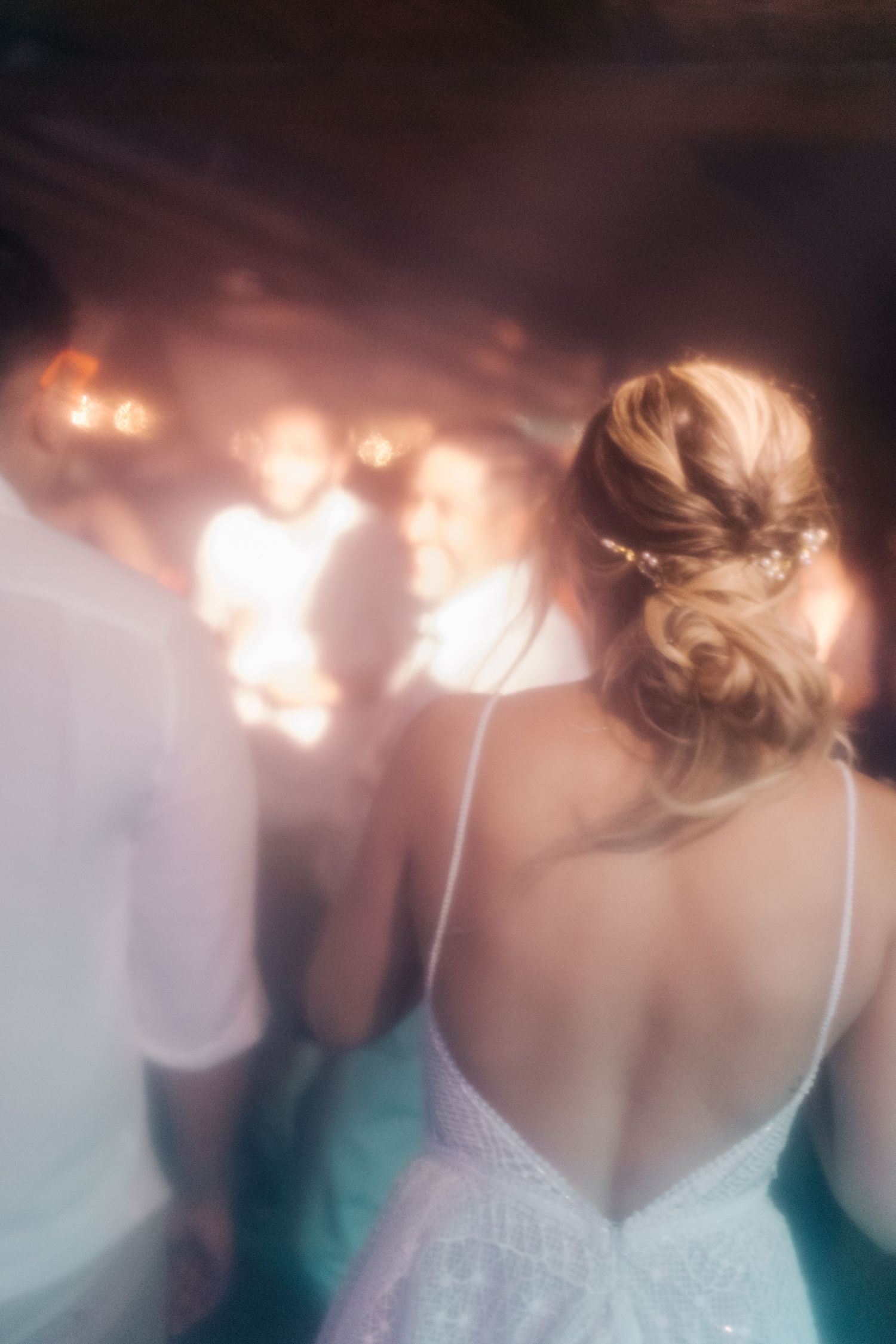 Back view of person in white lace dress dancing at dimly lit party.
