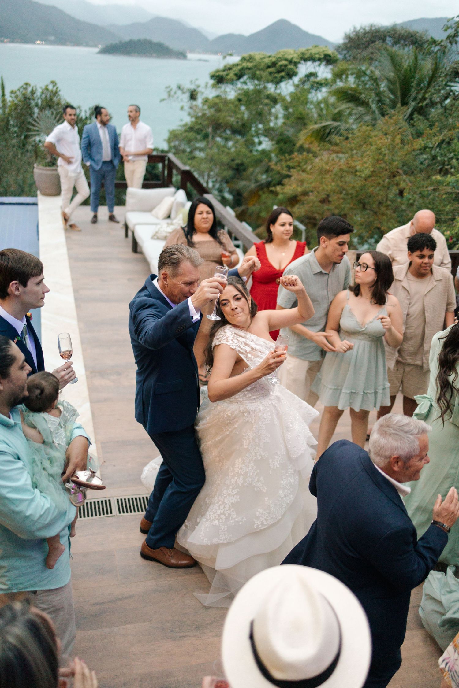 Wedding guests dancing together on an outdoor deck with mountain and ocean views.