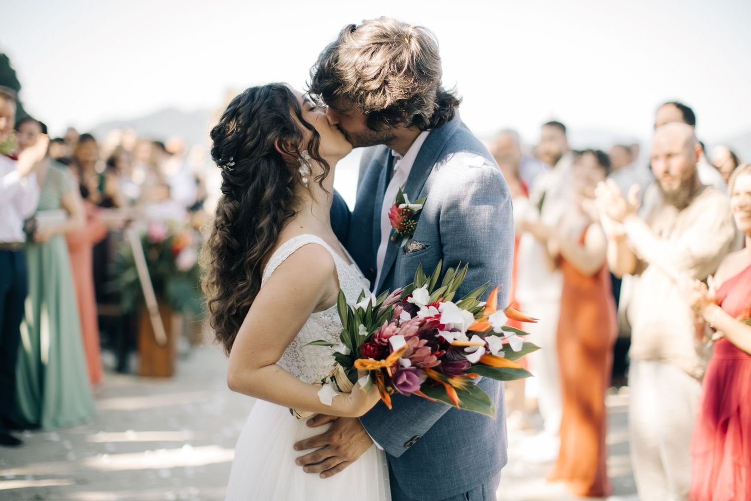 An intimate beach wedding celebration with guests cheering as the couple walks past.