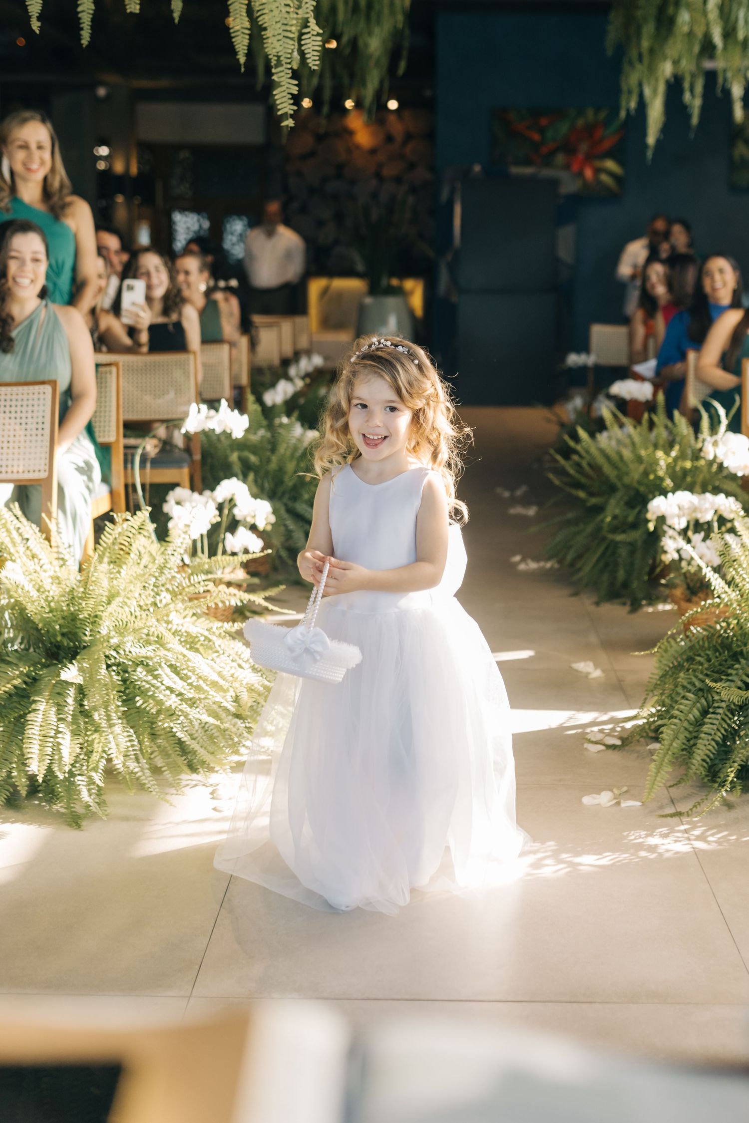 White-dressed attendants arranged along a sunlit aisle with ferns and floral decorations.