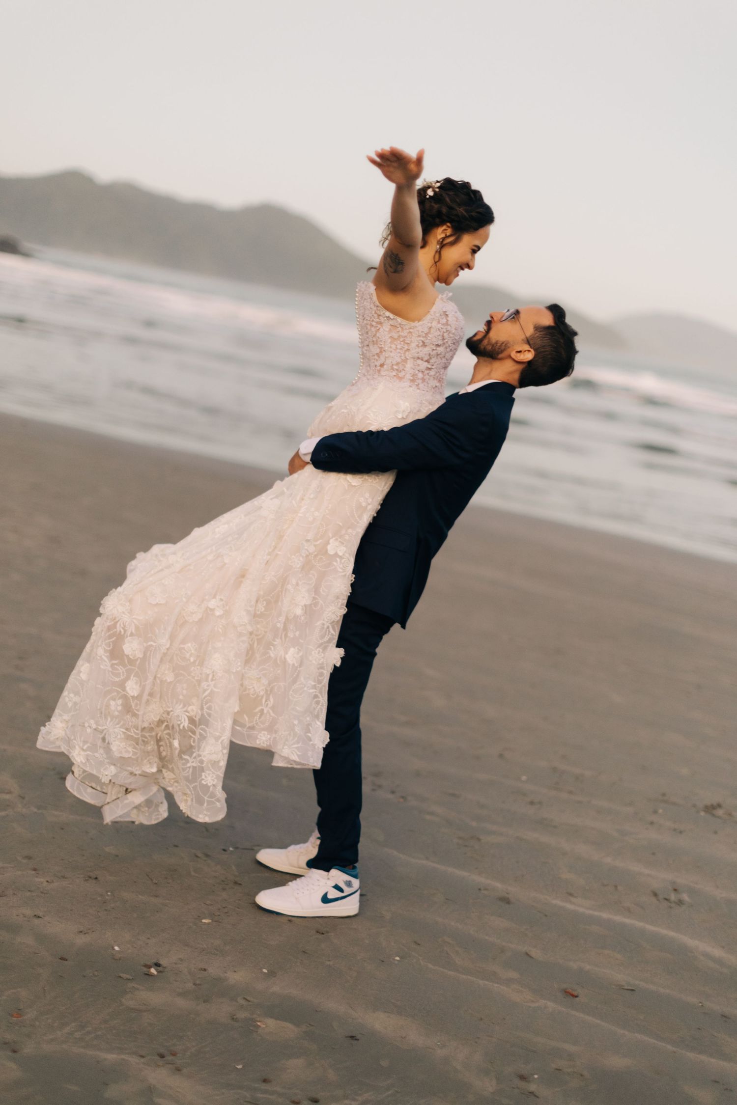 Playful wedding photo of a lift pose on the beach with mountains in the background.