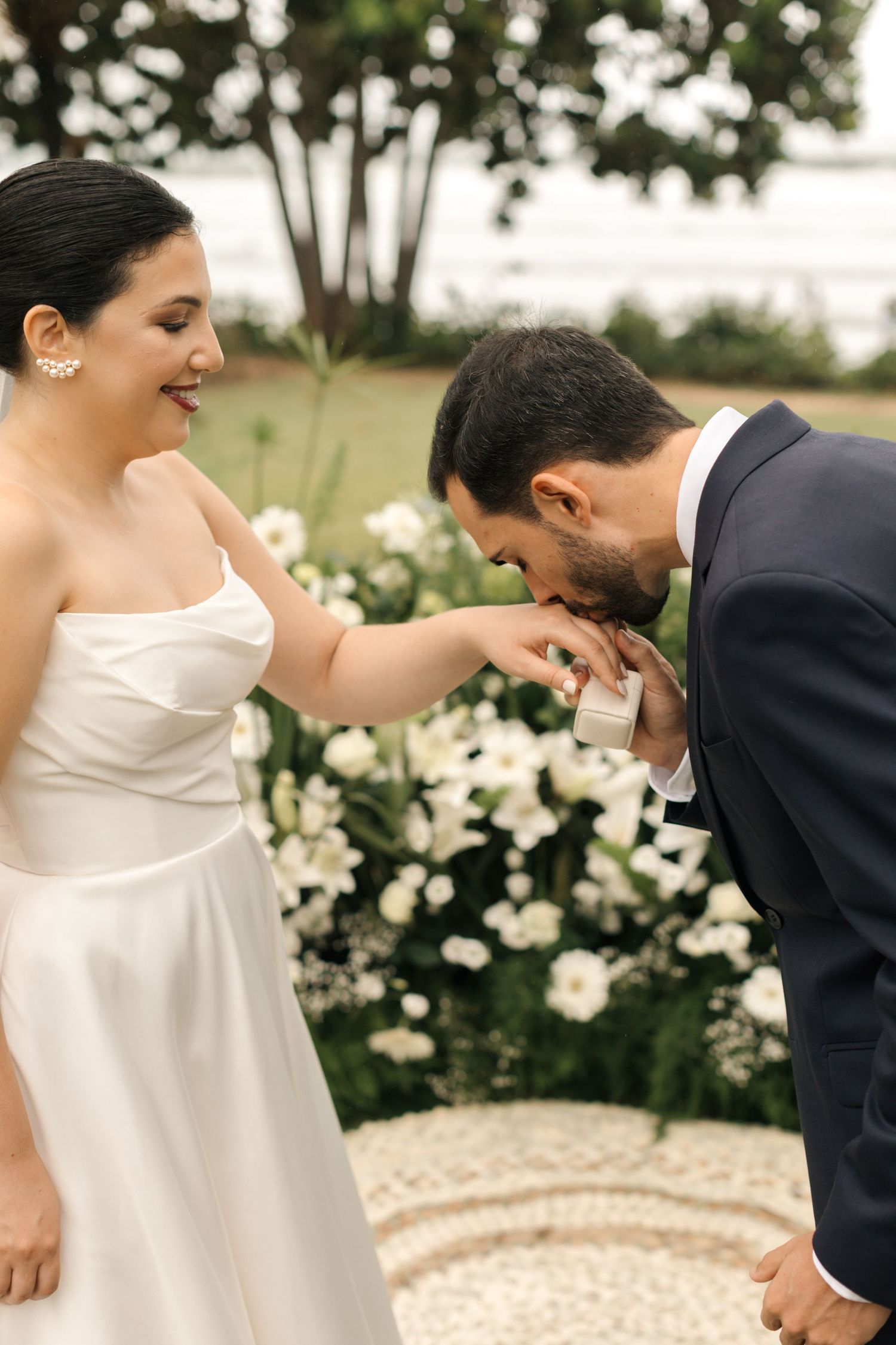 A tender moment during a wedding ceremony with a bride in white and groom in navy exchanging vows in a garden setting.