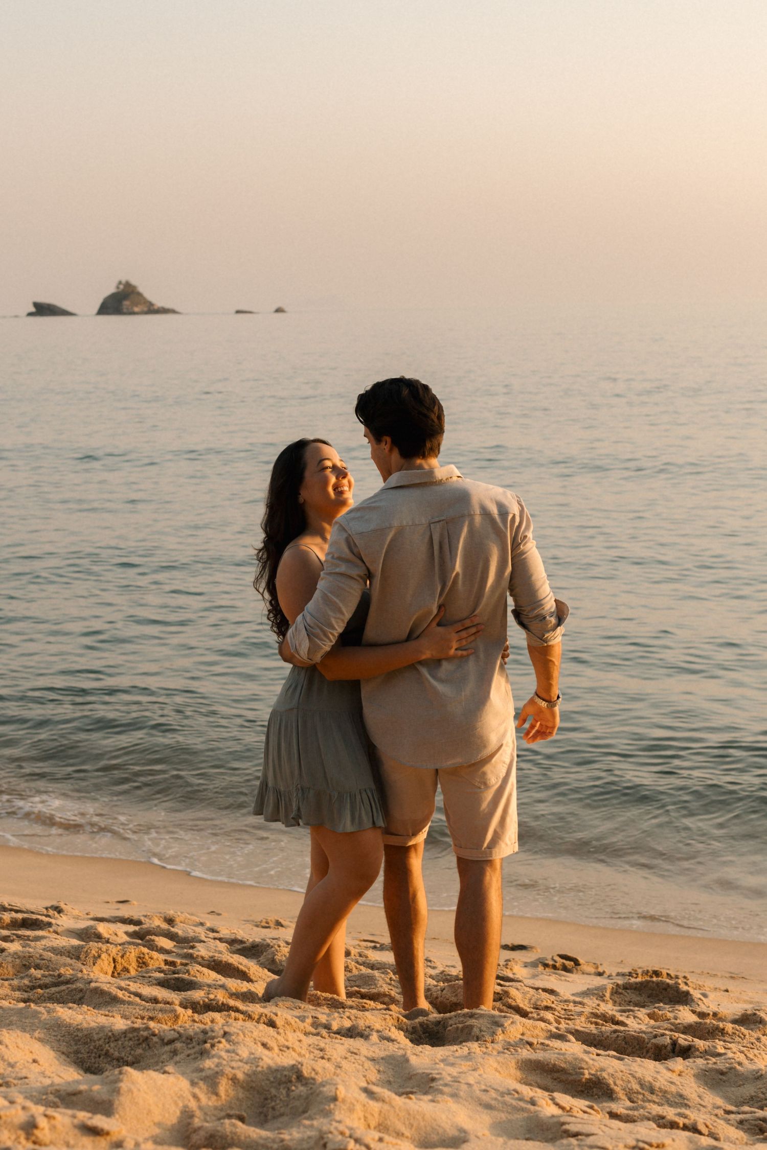 Couple embracing while looking out at the ocean during sunset.
