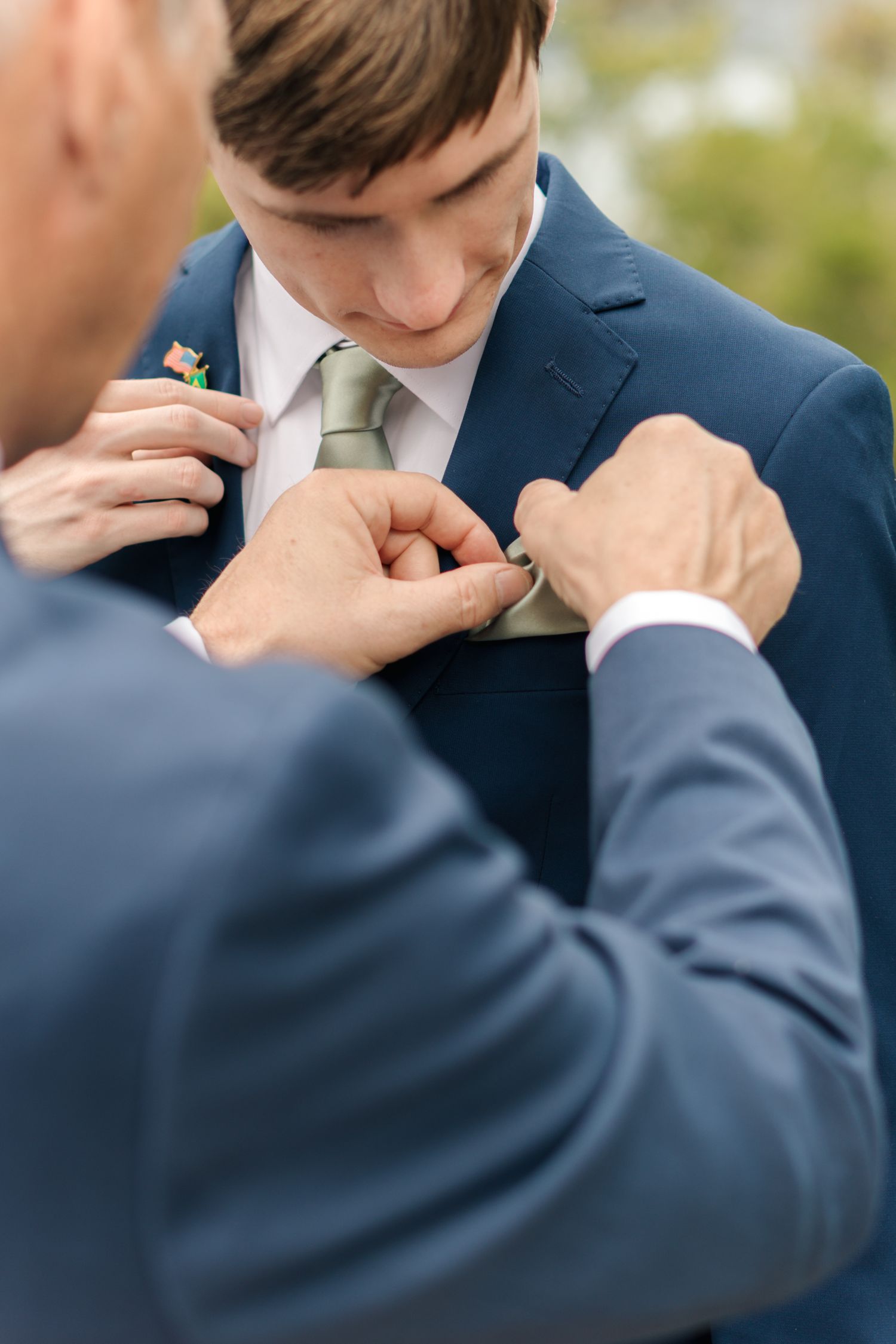 A close-up moment of adjusting a light colored tie on a navy blue suit during formal preparations.
