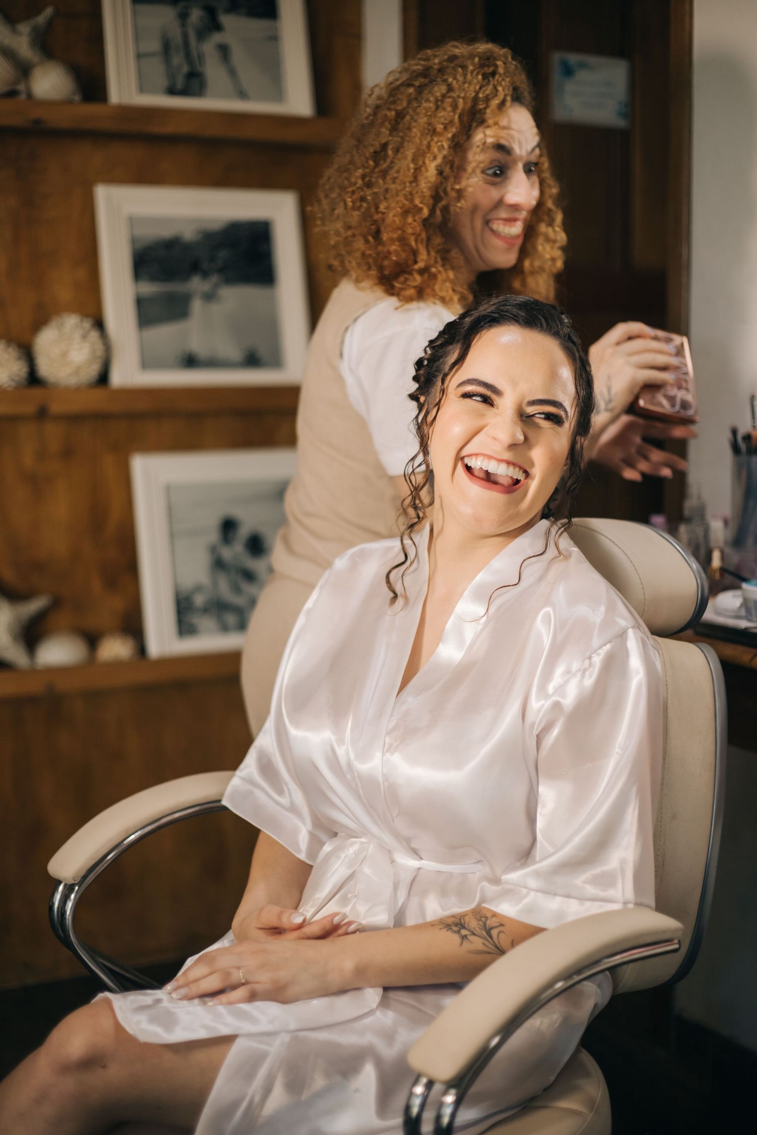 Wedding preparation scene with stylist working on bride's hair in white silk robe.