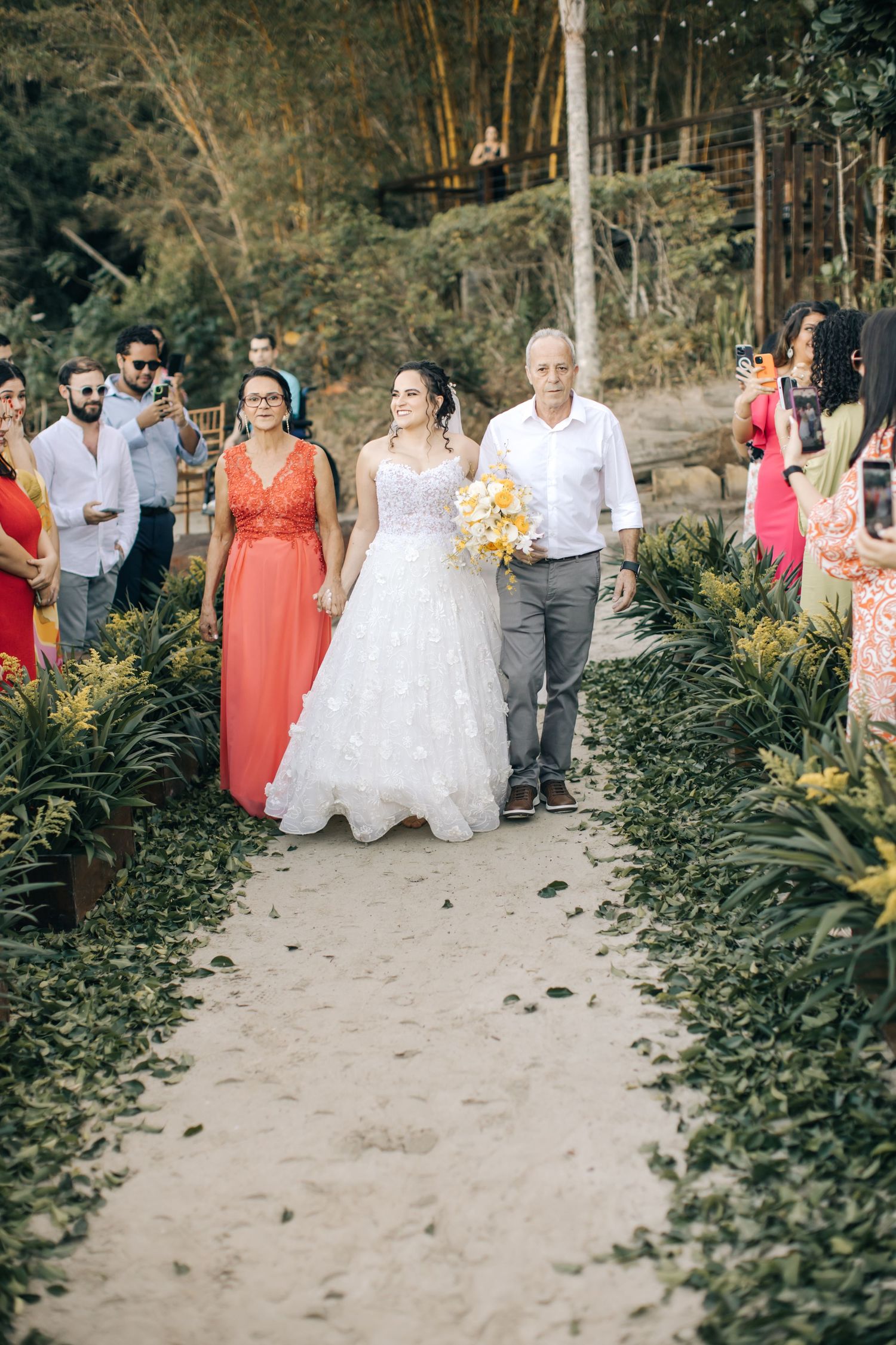 Wedding party walks down garden path lined with tropical plants.
