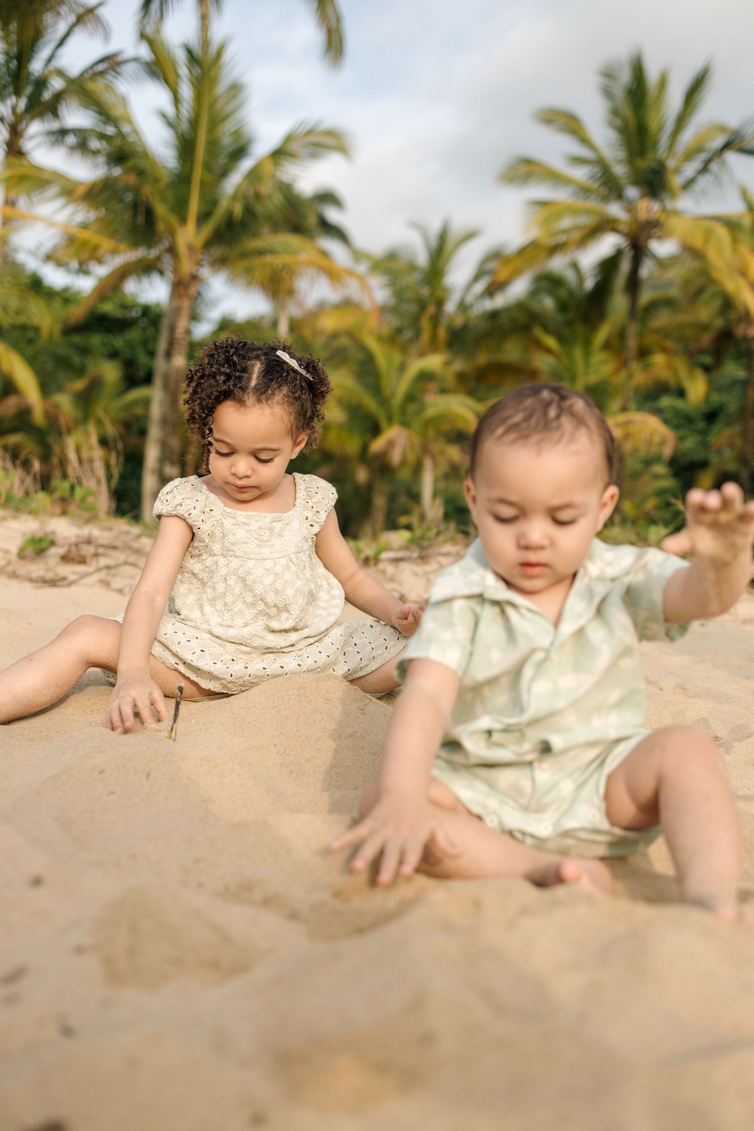 Young children playing in the sand on a tropical beach with palm trees in the background.