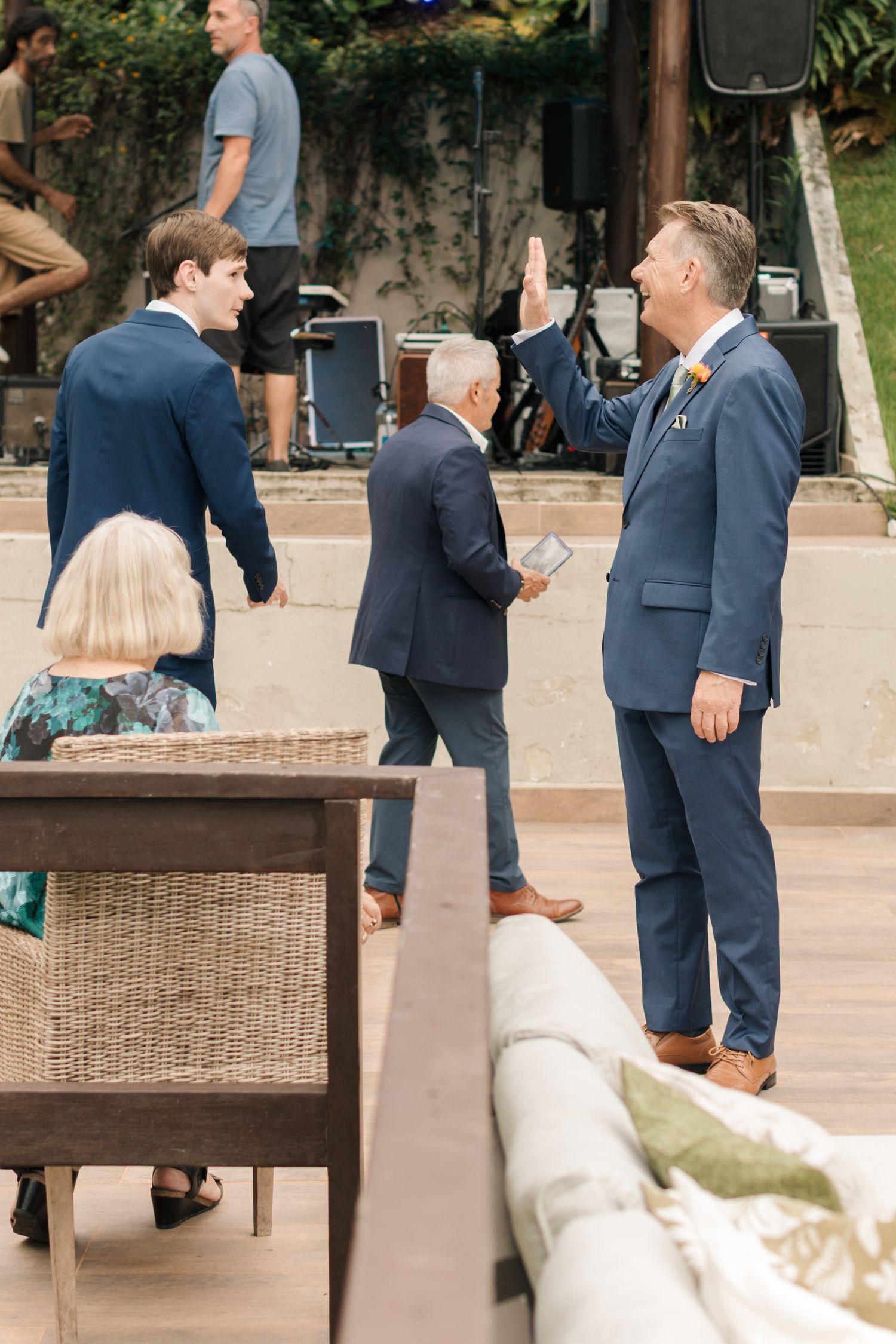 Guests in formal attire socializing at an outdoor event venue with patio furniture.