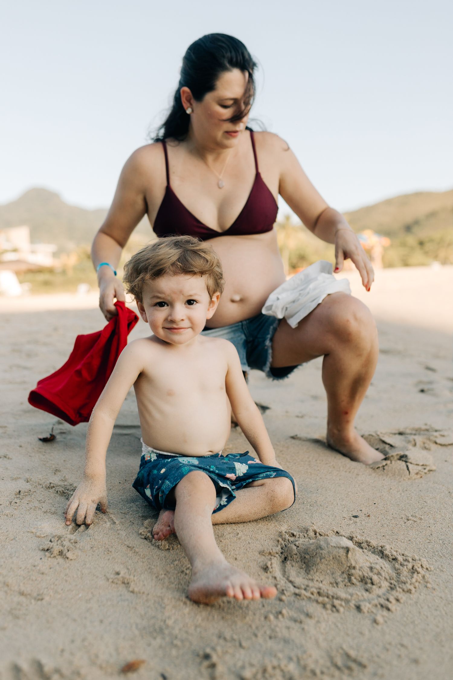 Mother and child playing together on a sunny beach with mountains in the background.