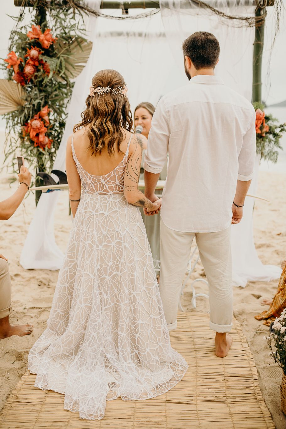 Back view of lace wedding dress as couple walks on wooden pathway at beach ceremony.