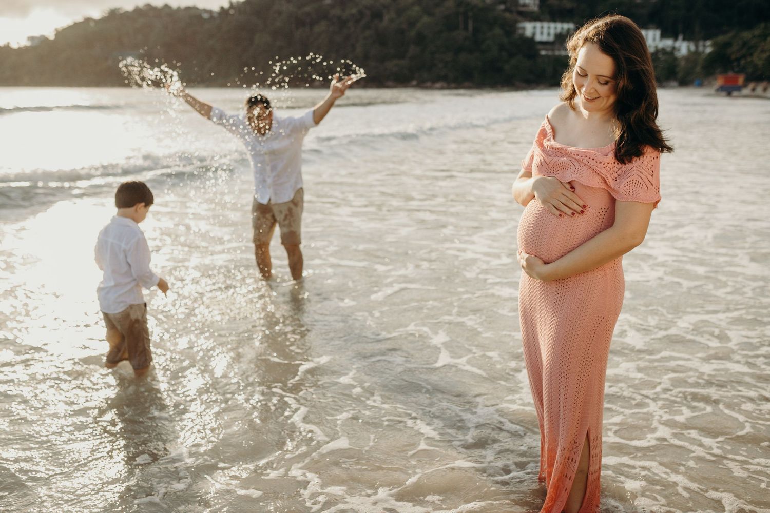 Family wading together in calm beach waters during golden hour.