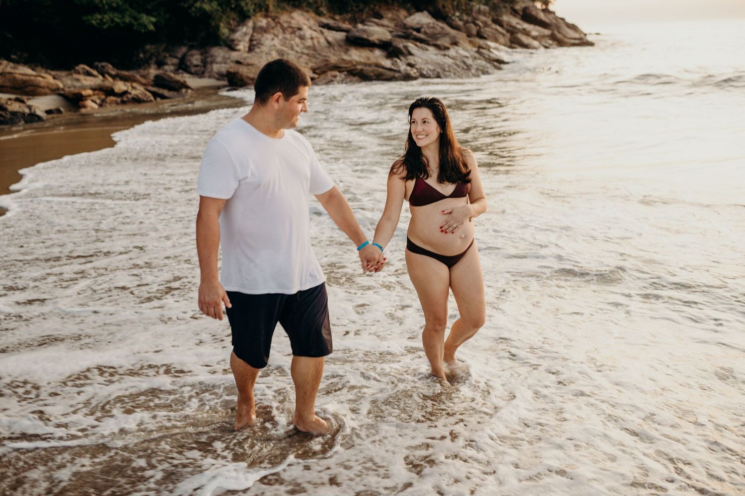 Family playing in ocean waves during sunset at scenic mountain beach.