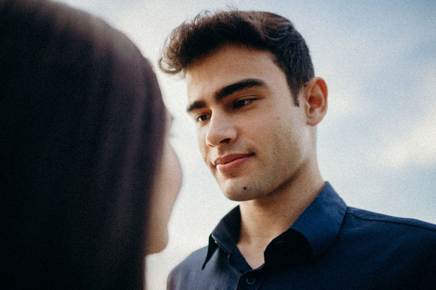 A close-up romantic shot of two people sharing a tender moment against a soft sky background.
