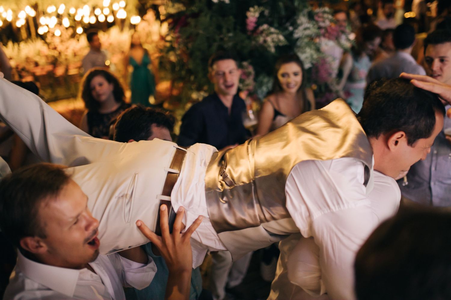 Wedding guests dancing enthusiastically under warm lighting during reception party.