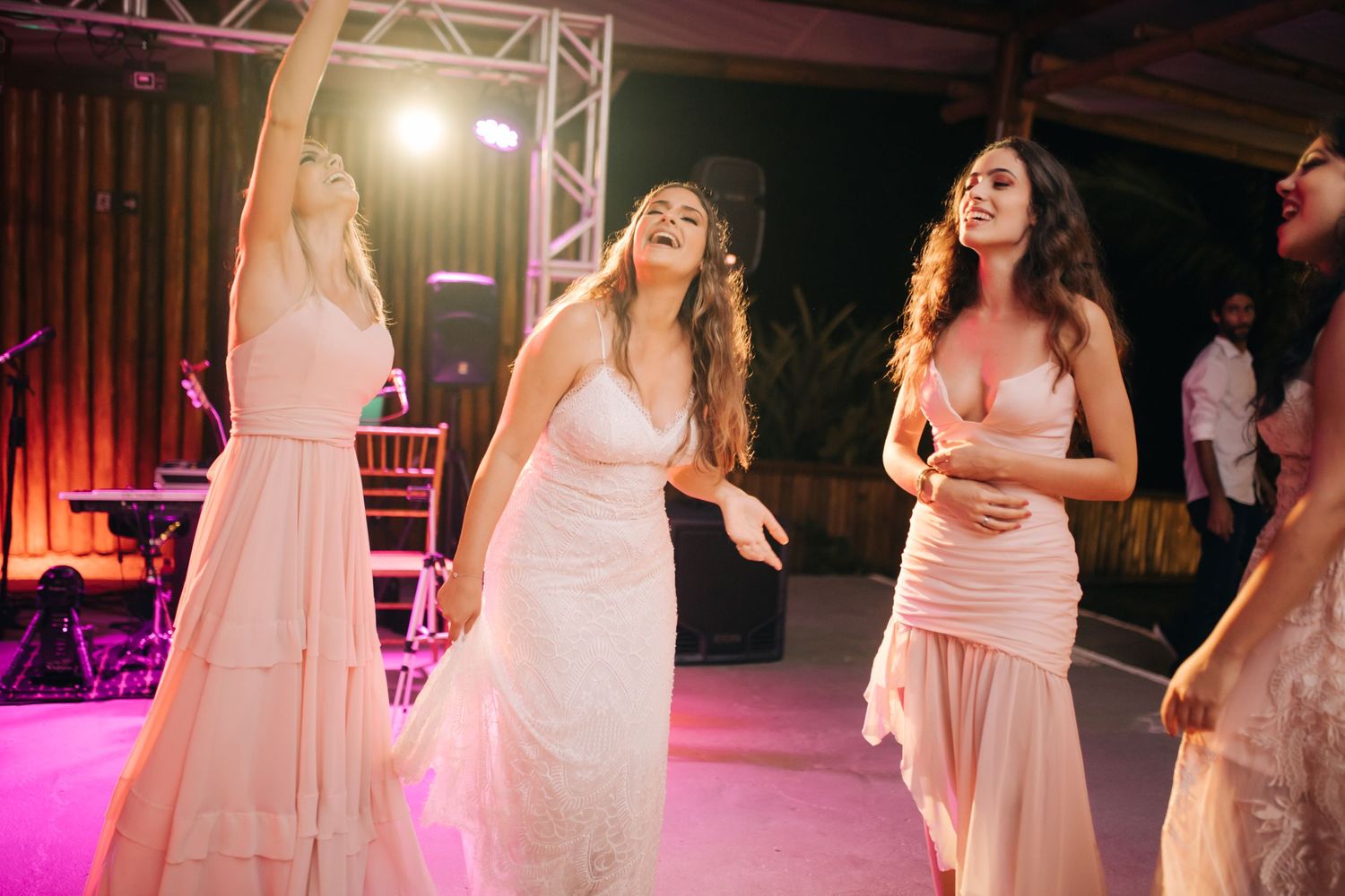 Wedding guests dance and celebrate on an illuminated dance floor with pink lighting.