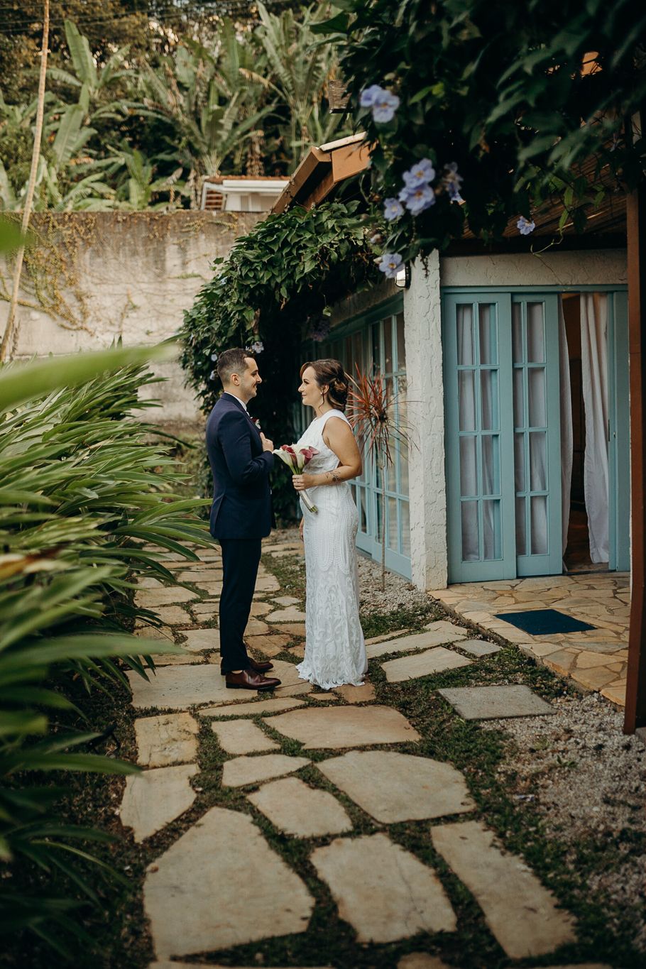 Couple standing together on stone pathway surrounded by lush garden vegetation.