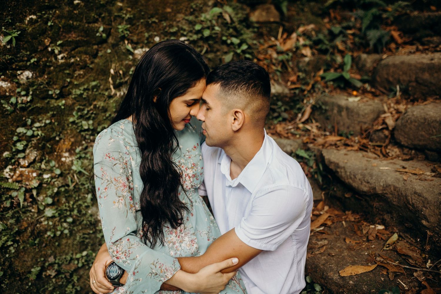 Couple embracing tenderly on rustic stone steps in a natural outdoor setting.
