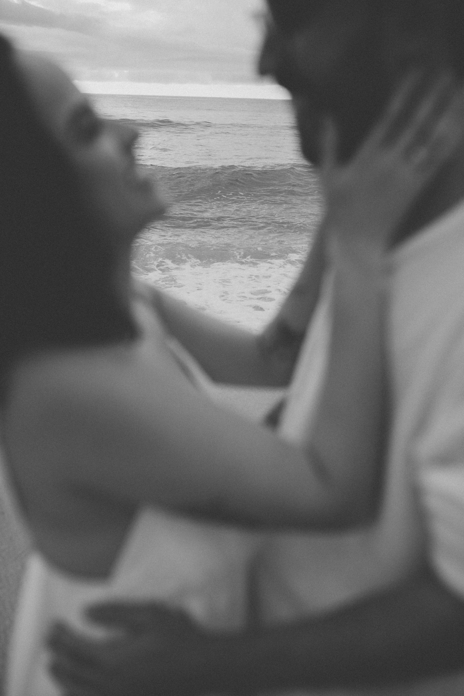 An intimate black and white portrait of a couple embracing by the ocean.