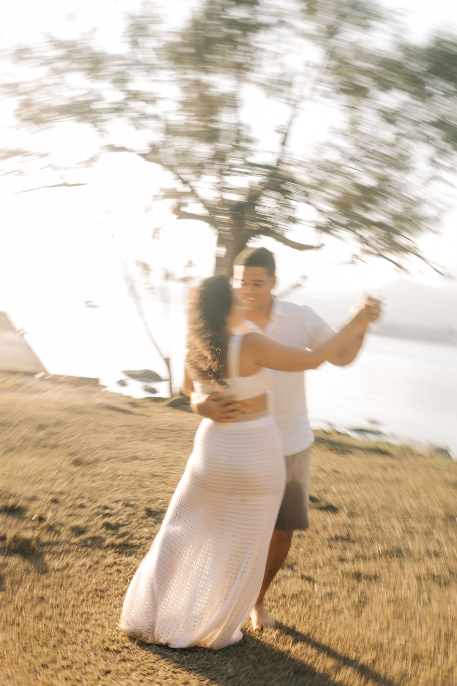 A couple dancing together on a grassy hillside during golden hour.