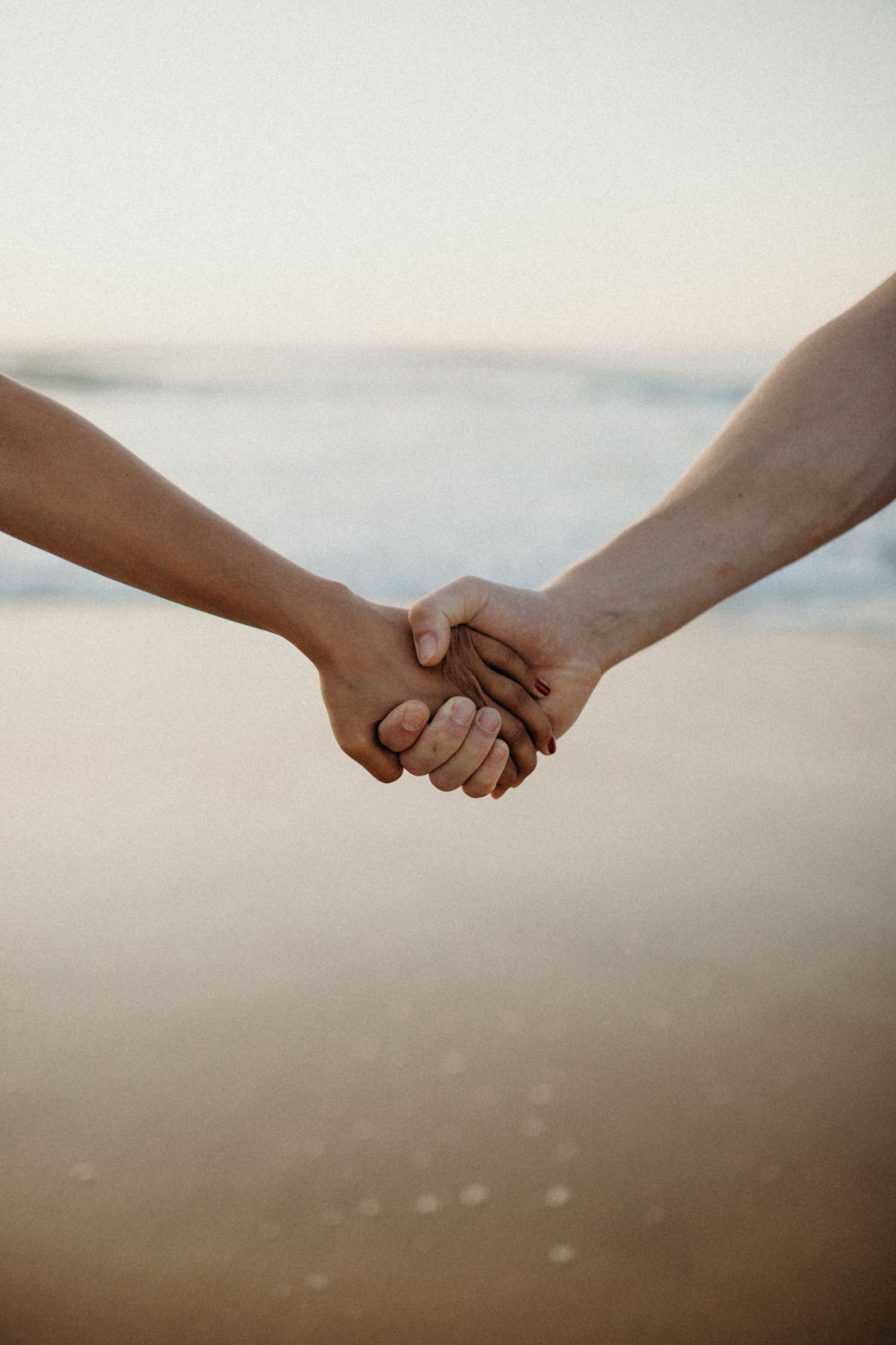 Close-up view of two hands clasped together against blurred beach background at sunset.