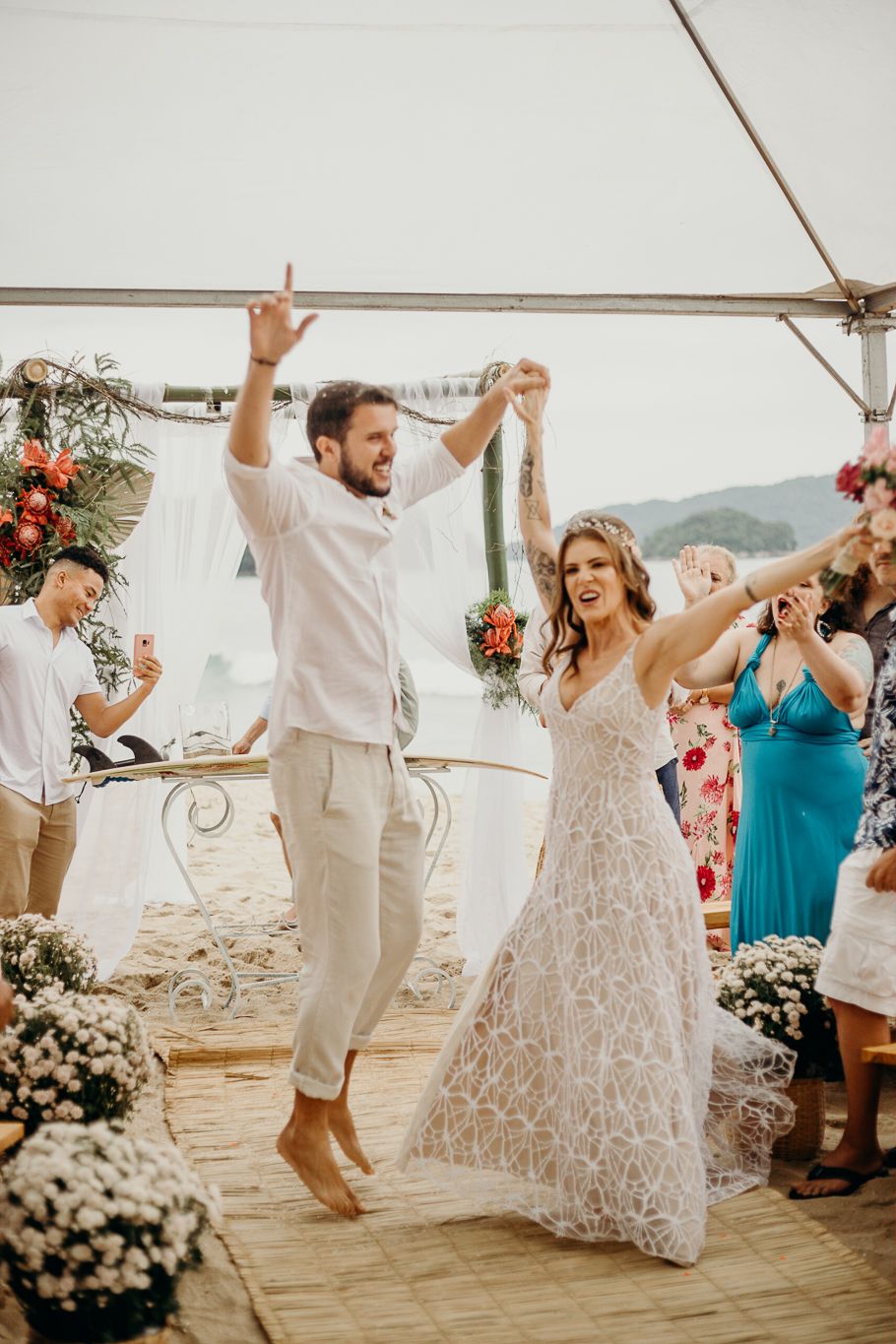 Wedding celebration with guests dancing and raising their arms in joy under a beachside tent.