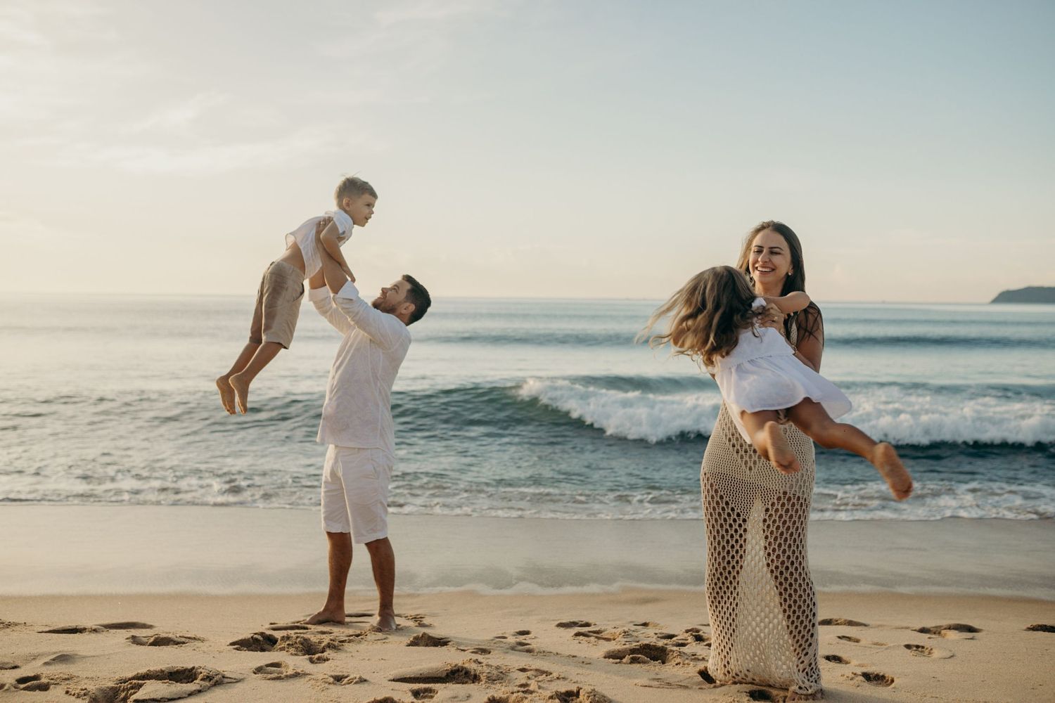 Family playing and lifting children on beautiful beach during sunset.