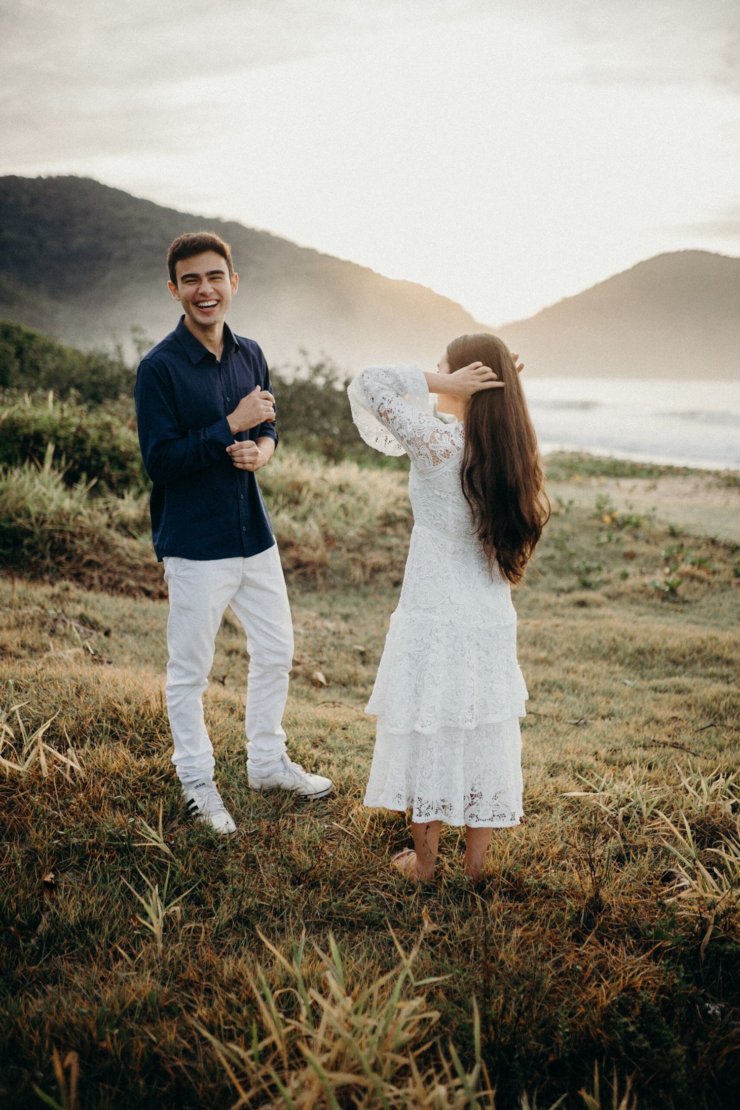 Couple in coordinated white and navy outfits enjoying a scenic coastal mountain view.