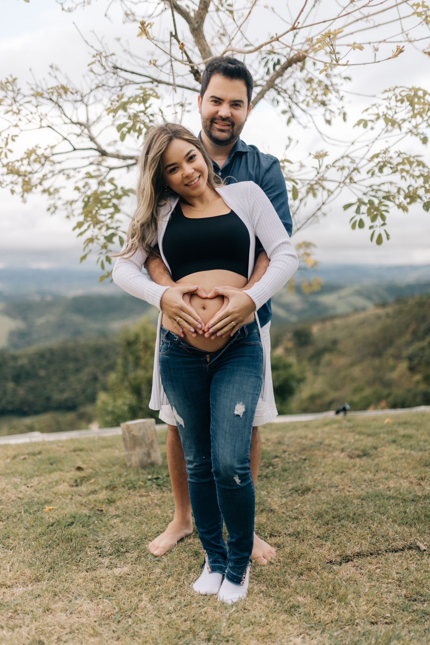 A couple embracing on a grassy hilltop with scenic mountain views in the background.