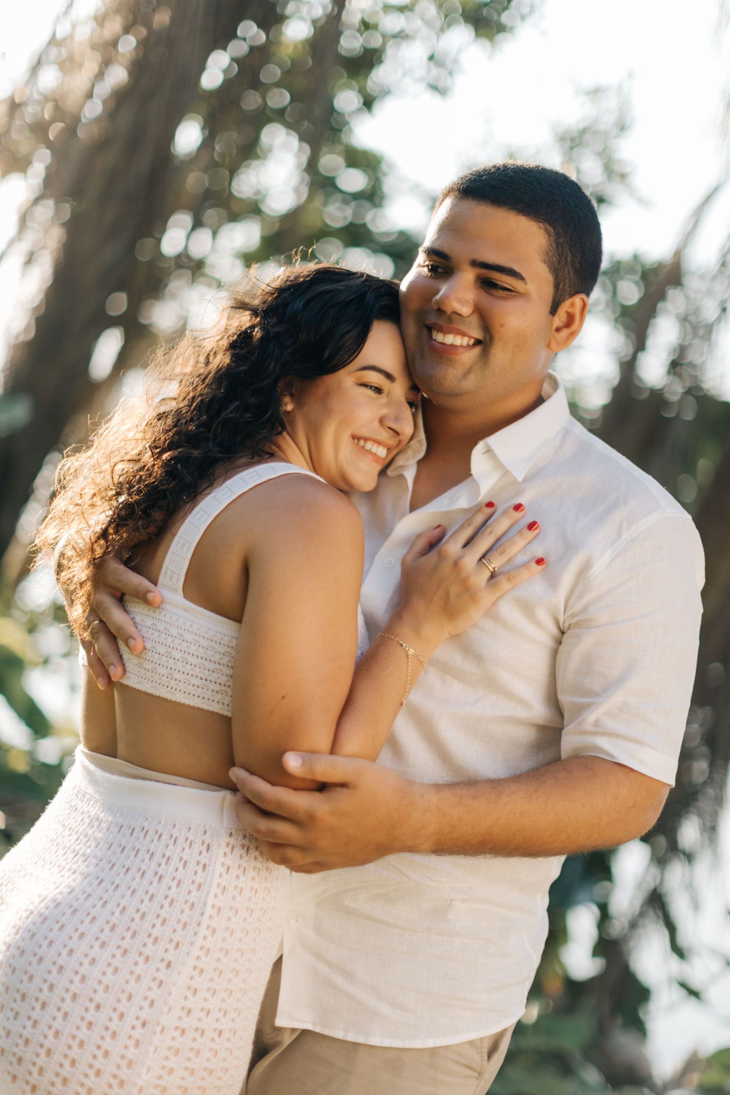 Couple in coordinating white outfits laugh together during outdoor photo session.