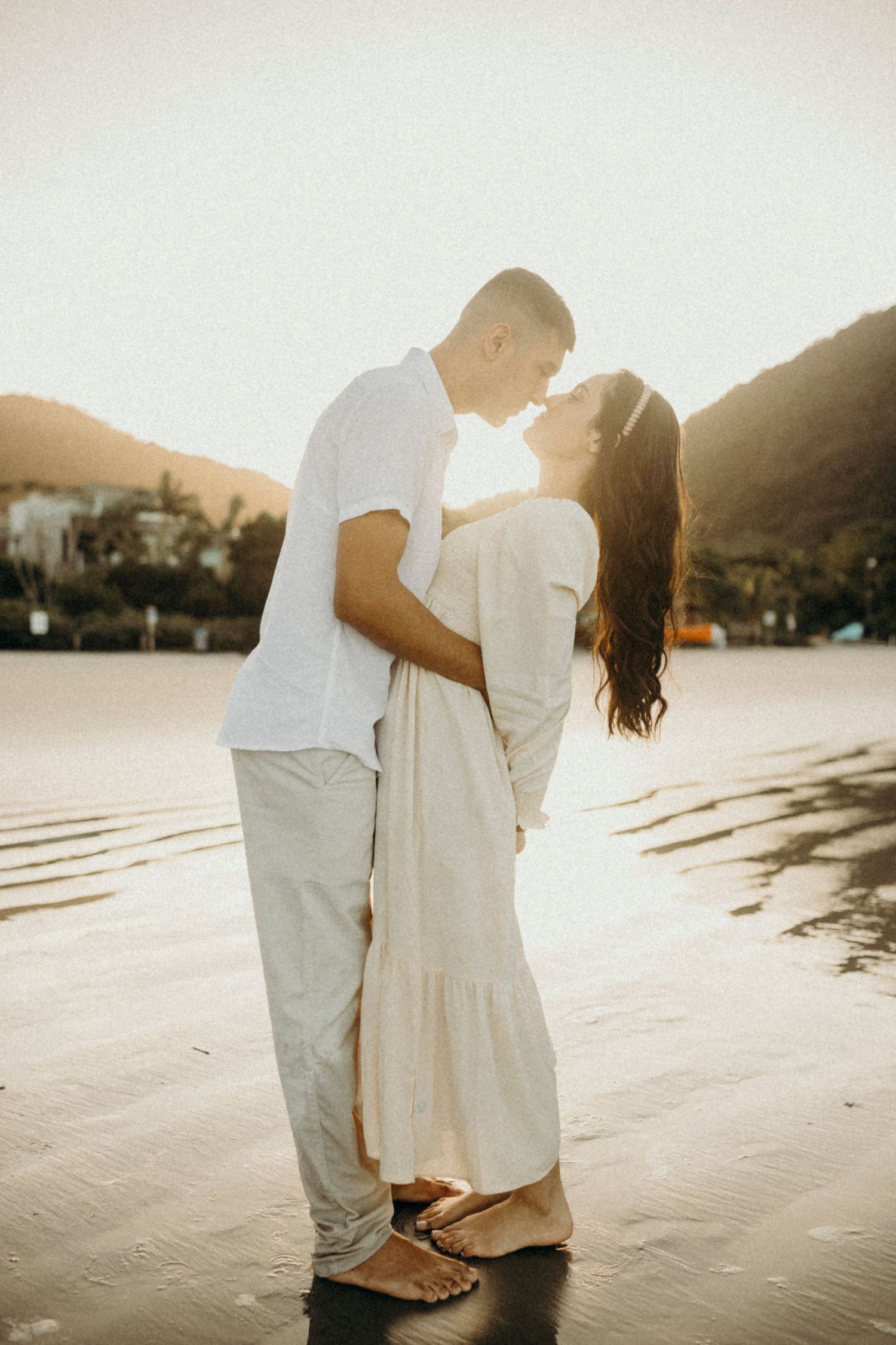 Romantic sunset beach photo of couple in white and cream outfits gazing at each other.