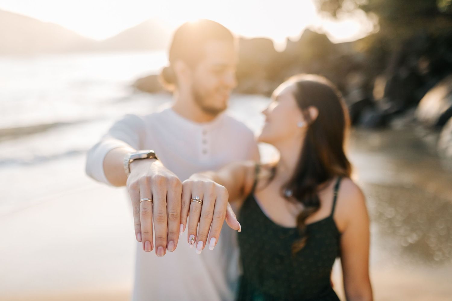 Engagement ring shown in close-up with couple on sunny beach.