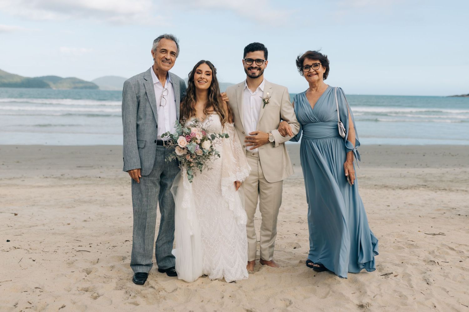 Beach wedding party in mix of blue and white attire pose together by the ocean.