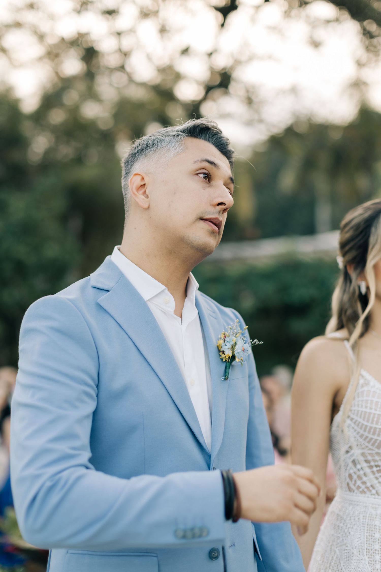 Groom in powder blue suit with boutonniere at outdoor wedding.