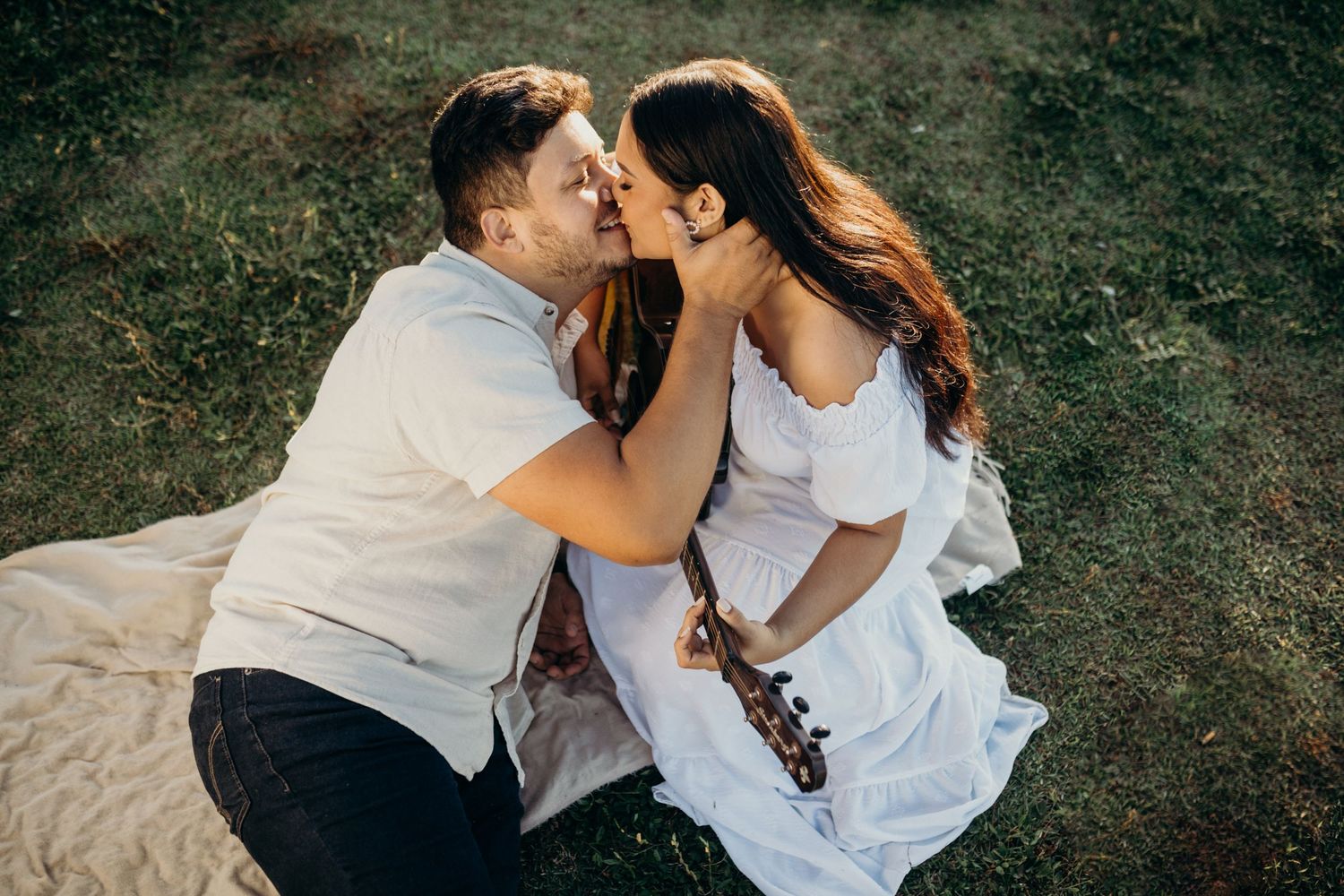 Intimate outdoor moment between couple sitting on picnic blanket at sunset.