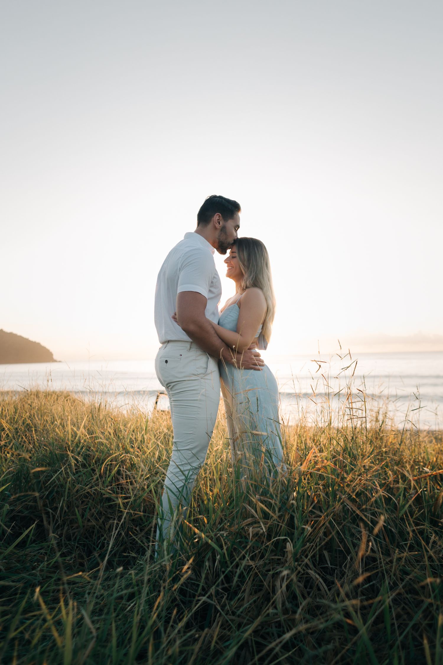 Intimate moment between couple standing in tall beach grass during sunset.