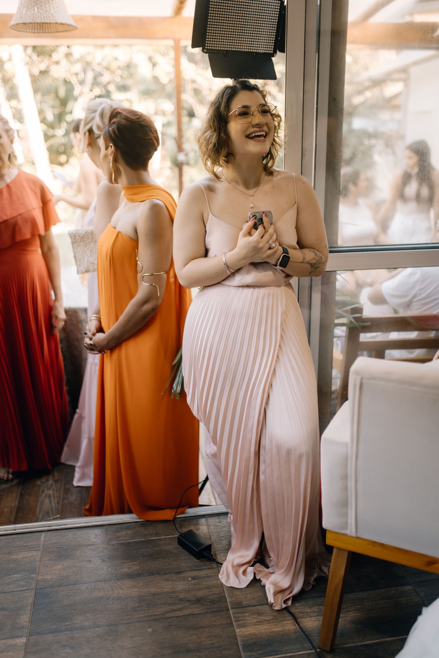 Bridesmaid in pleated blush gown laughs joyfully during wedding celebration.